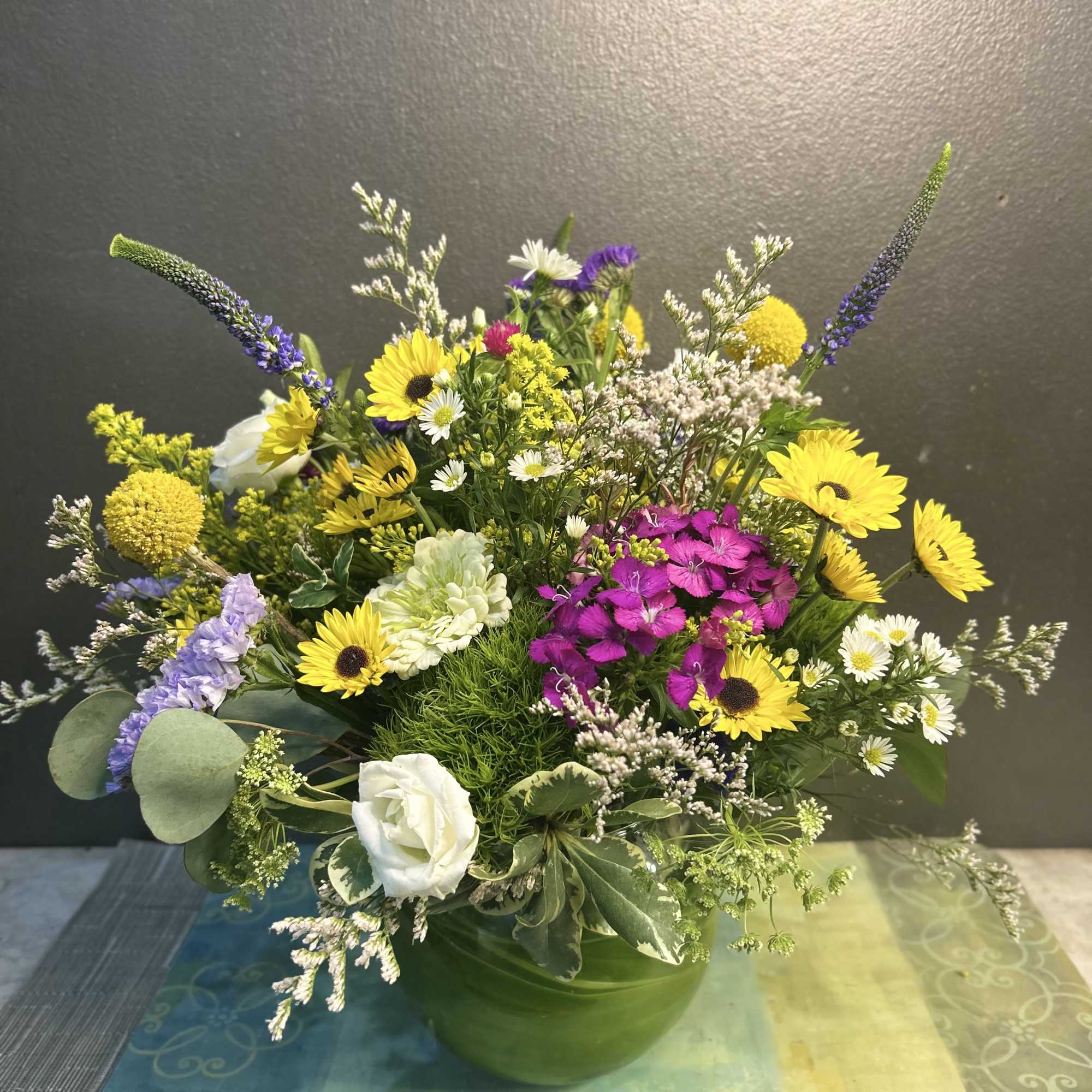 Mixed bouquet in a green vase with yellow, purple, white, and pink flowers