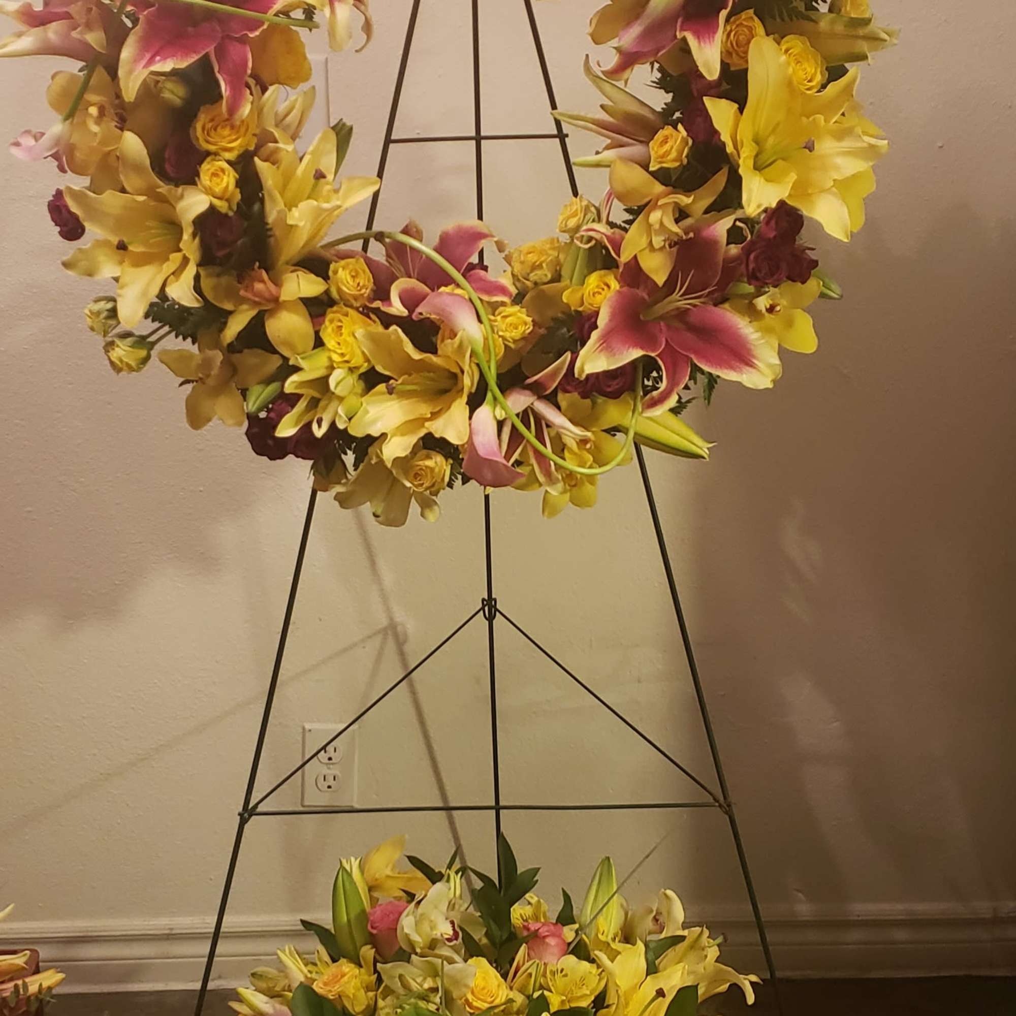 Large floral wreath on a black stand with yellow lilies and pink flowers