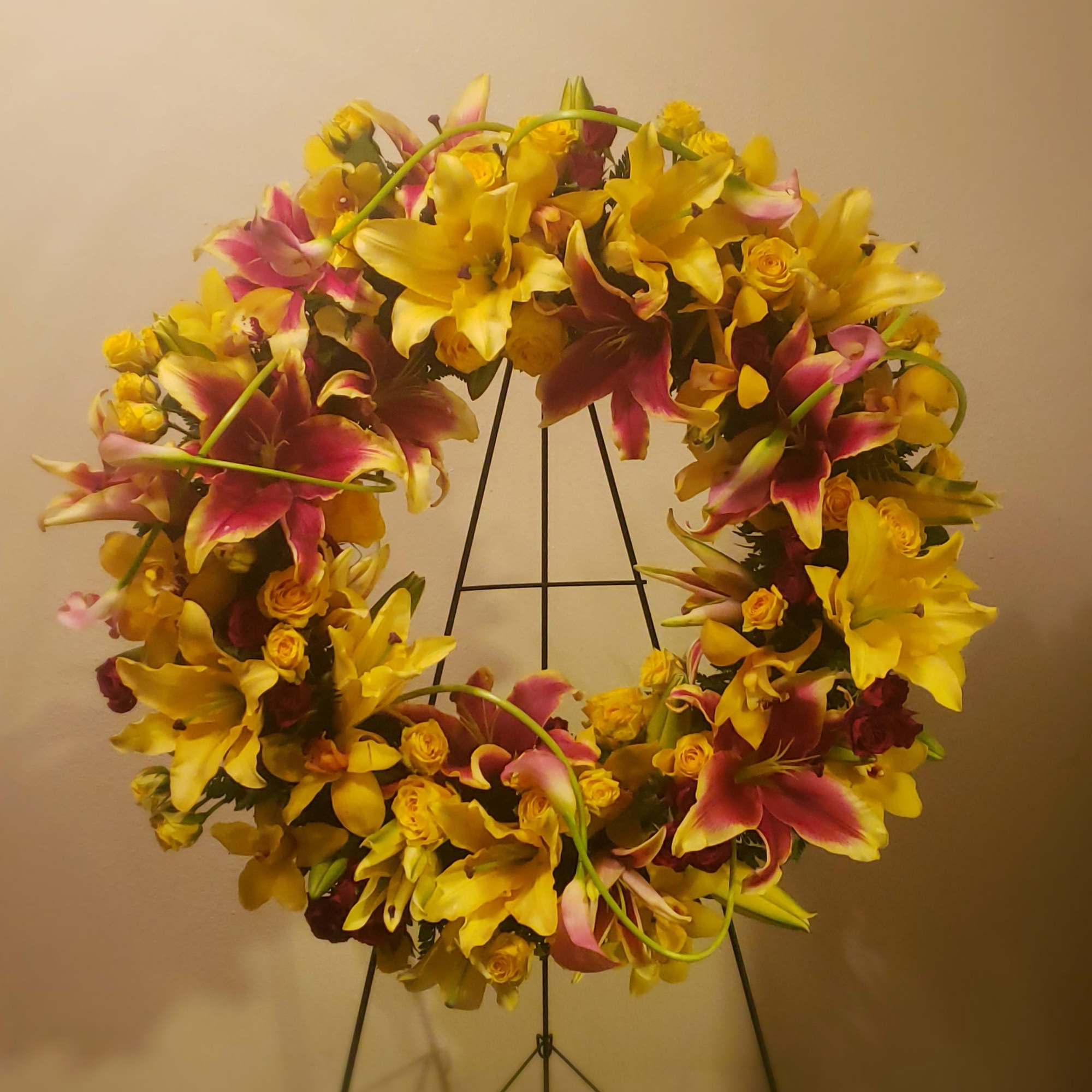Large floral wreath of yellow and pink lilies on a metal stand