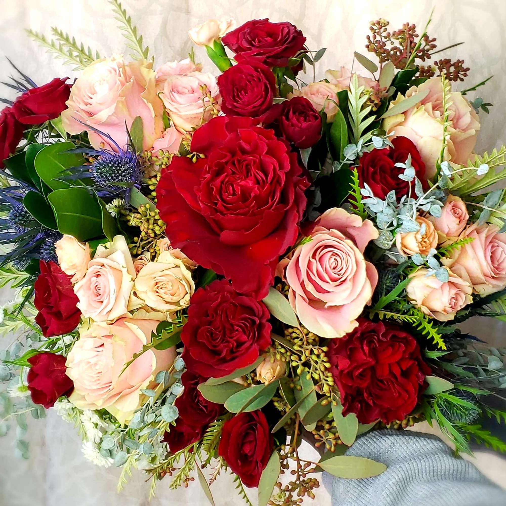 Bouquet of red and blush roses with blue thistle accents