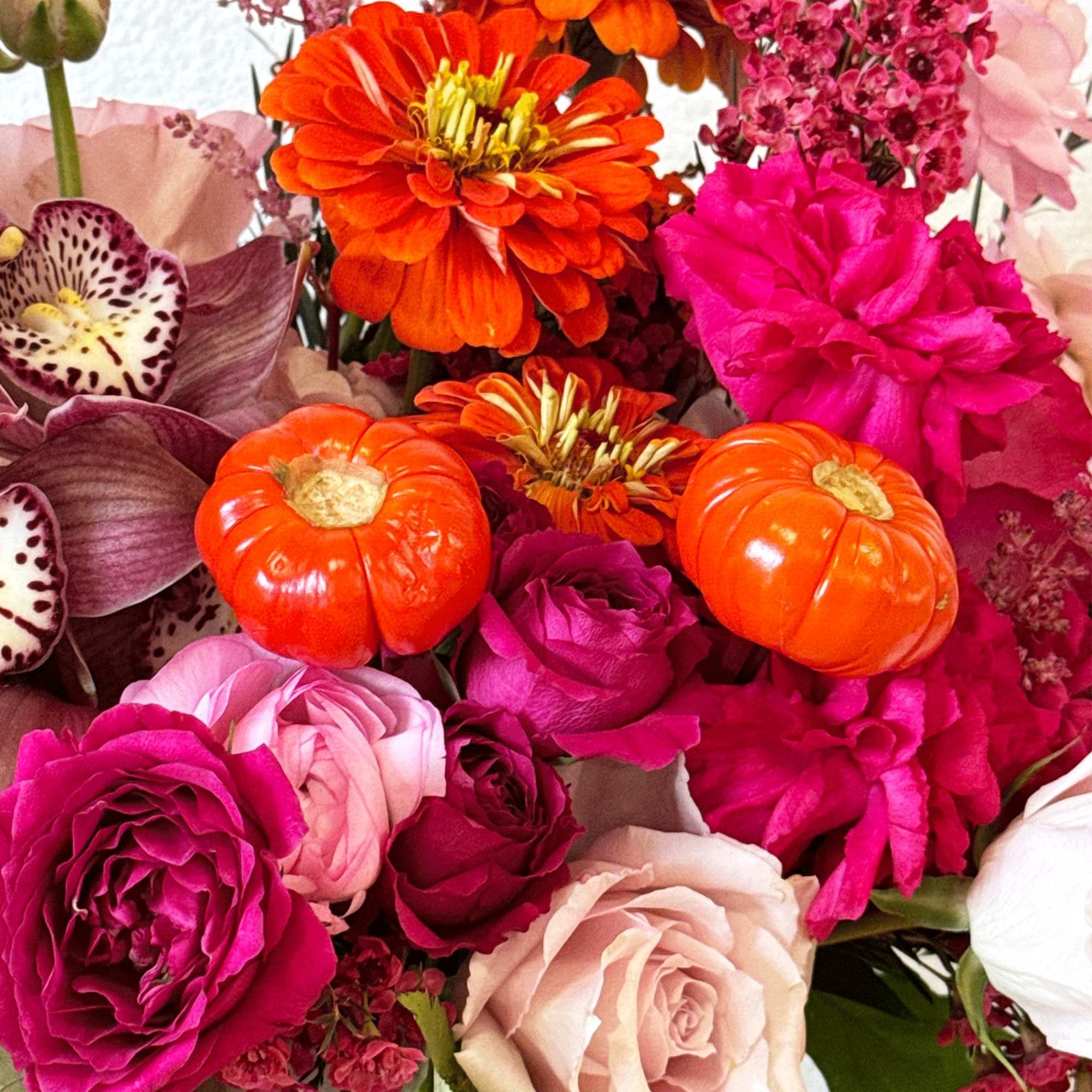 Bright mixed bouquet with orange blooms, pink roses, and small pumpkins