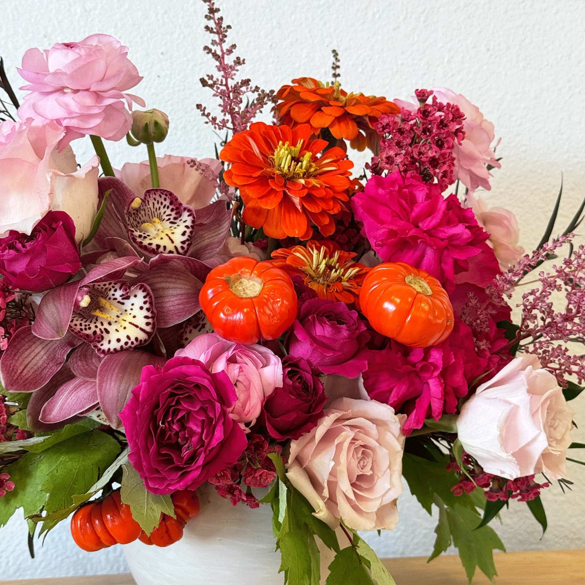 Mixed bouquet of pink, orange, and magenta flowers with small pumpkin accents