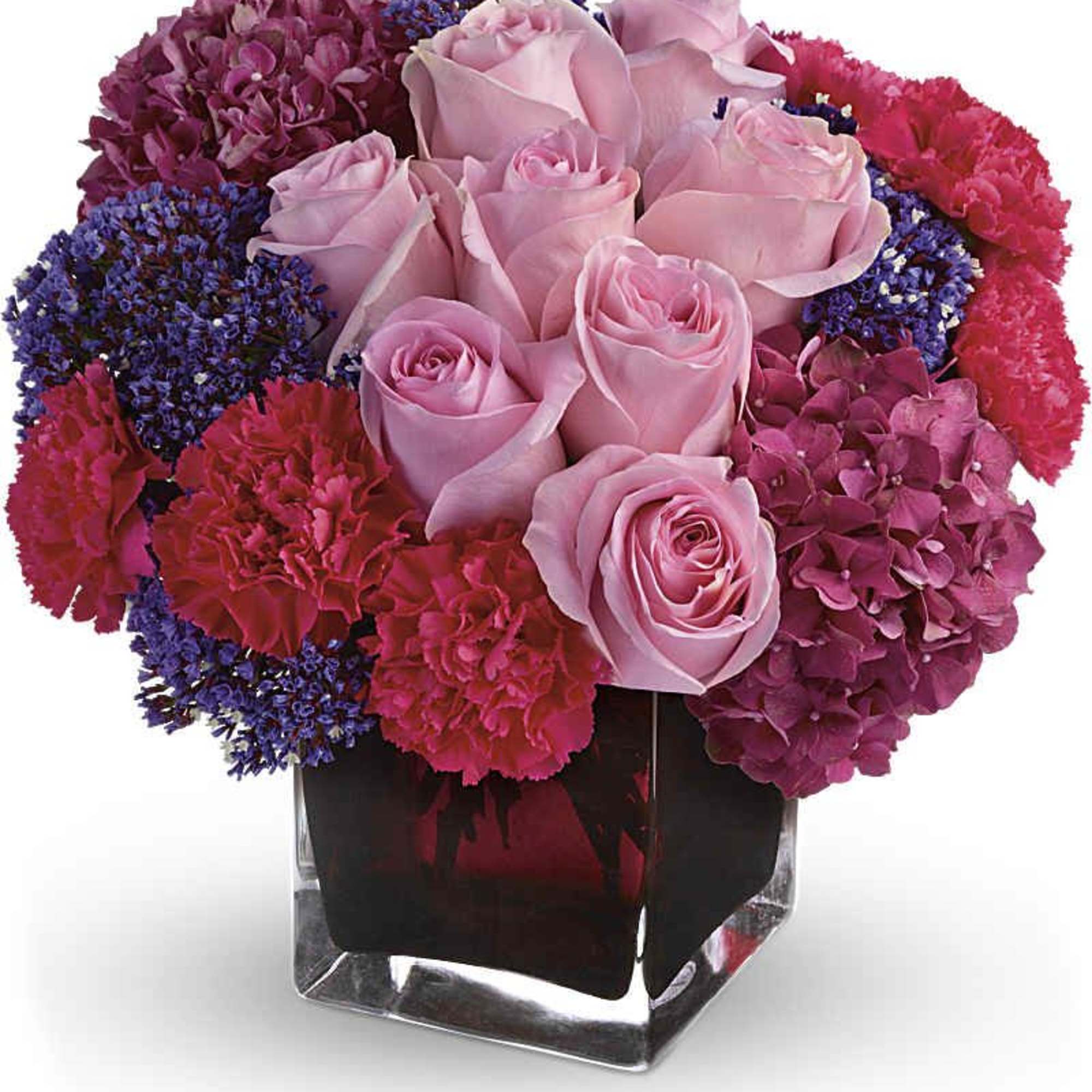 Compact mix of pink roses, red carnations and purple flowers in a square glass vase