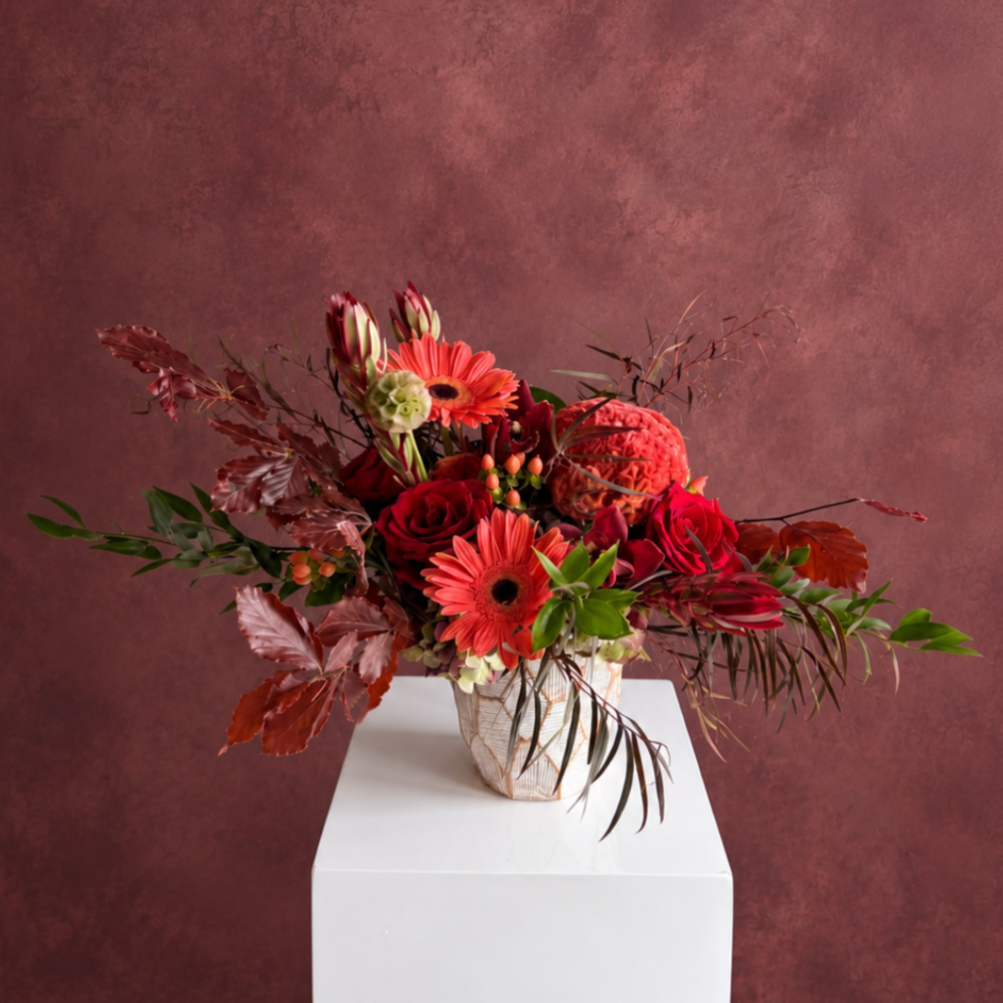 Red floral arrangement in a white vase on a pedestal