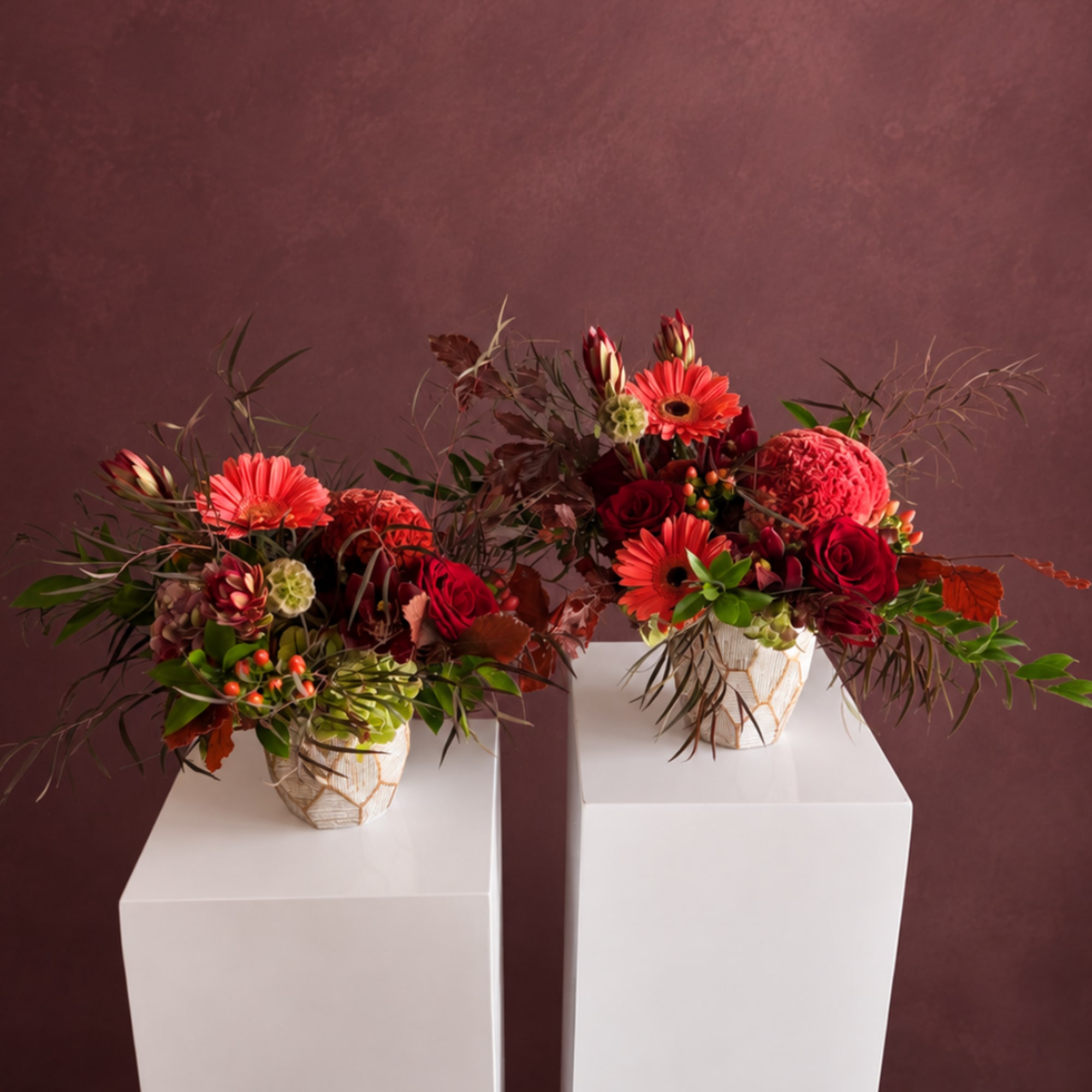 Two red floral arrangements in white vases on pedestals
