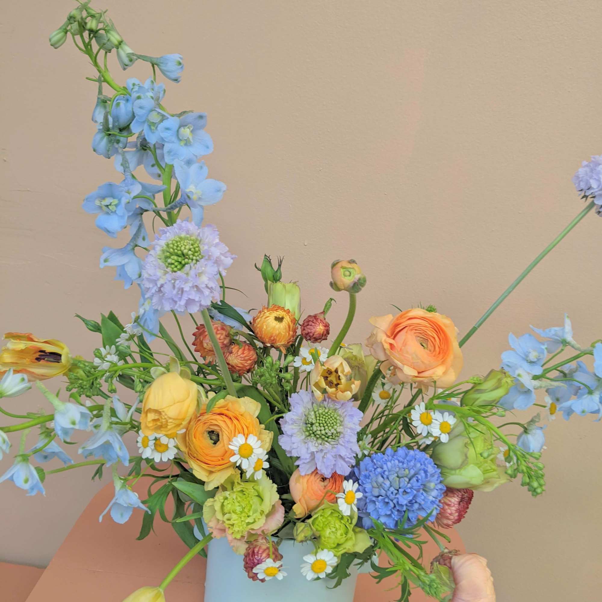 Mixed pastel bouquet in a light blue vase with tall blue blooms