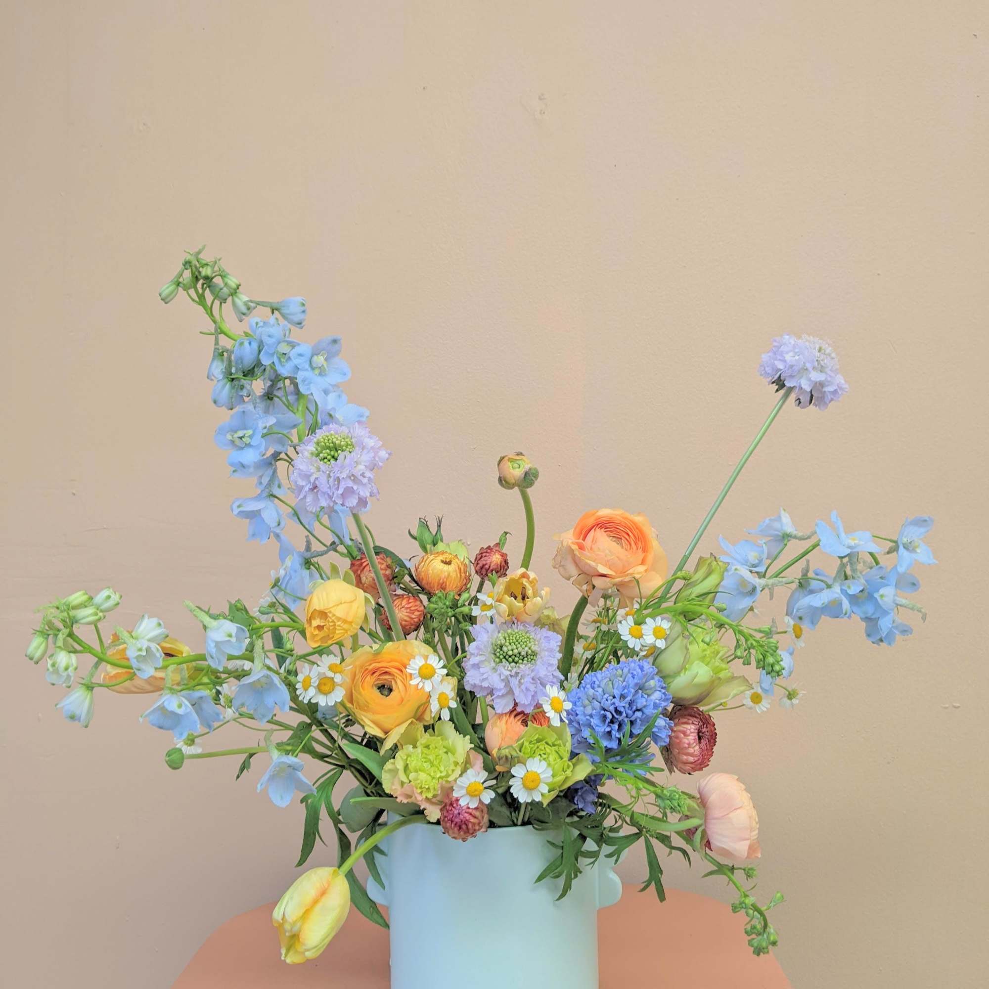 Pastel mixed bouquet in a light blue vase with blue and yellow blooms