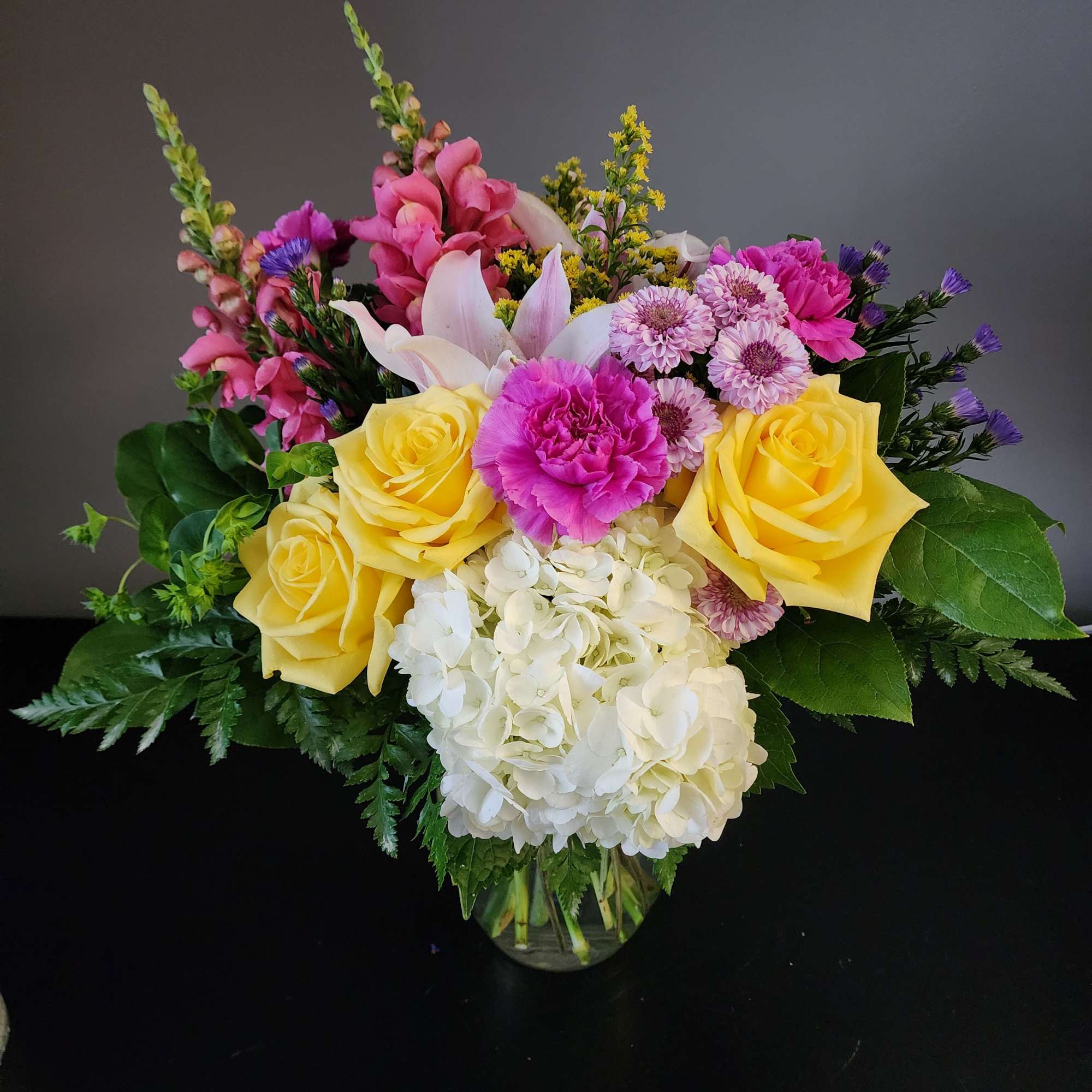 Mixed bouquet of yellow roses, pink blooms, and white hydrangea in a glass vase