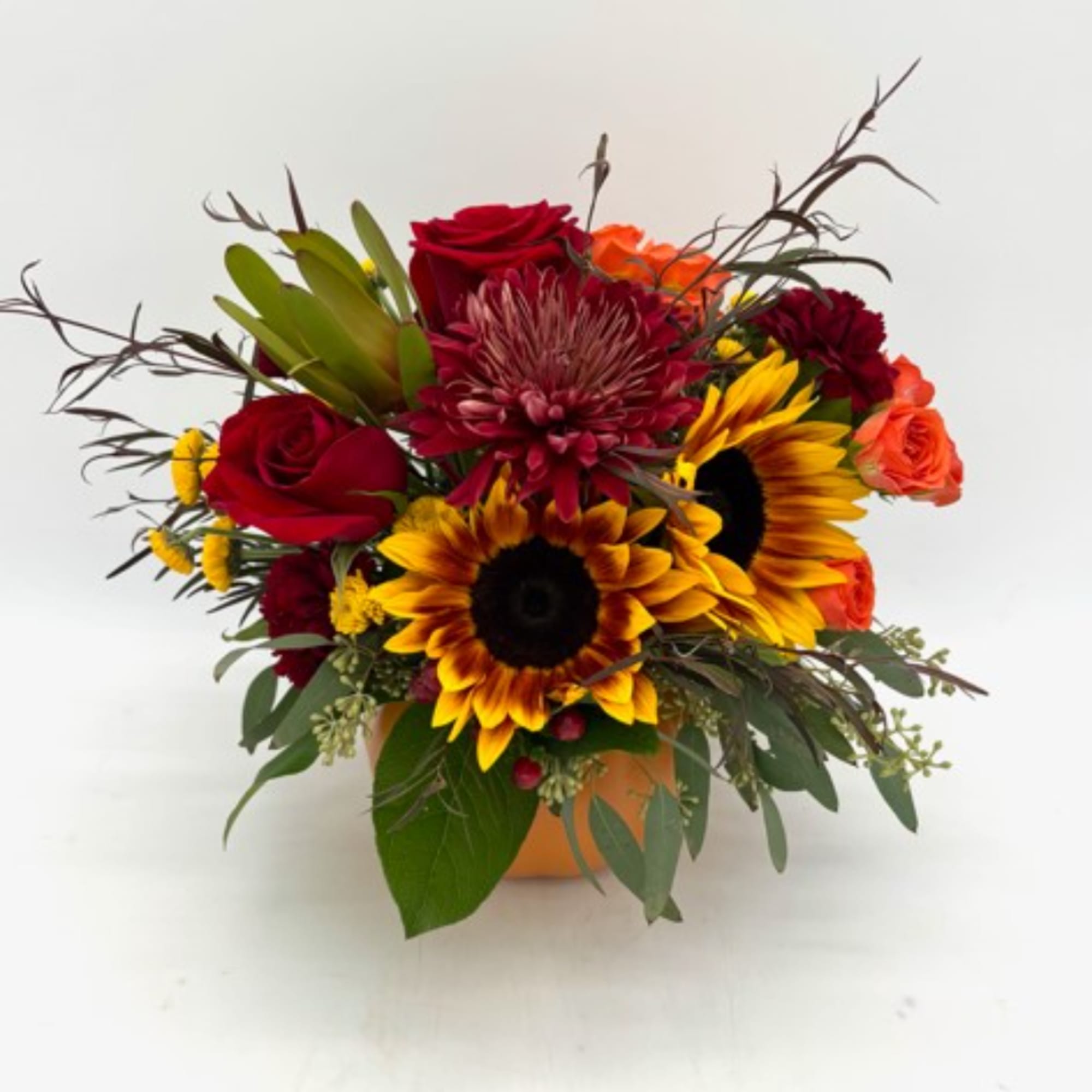 Mixed bouquet with red roses and sunflowers in a low orange container