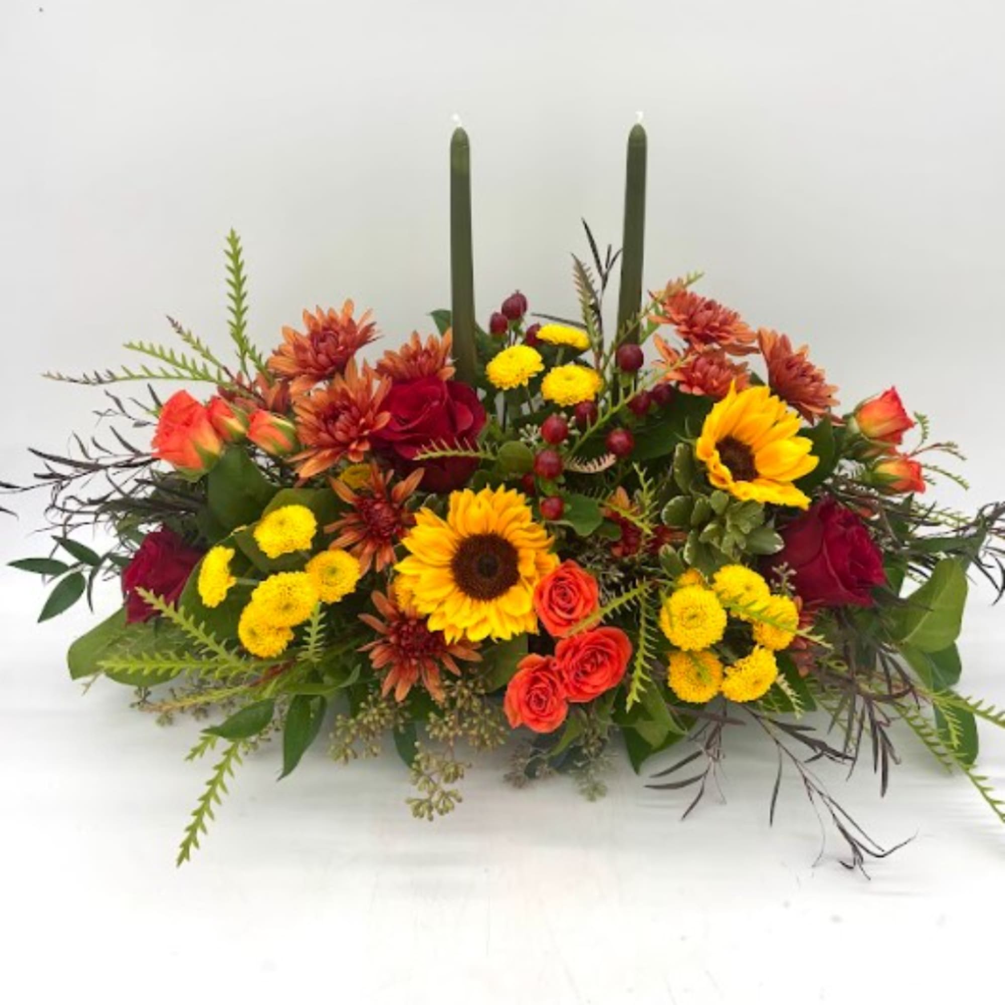 Low floral centerpiece with sunflowers, red roses, and yellow mums in a long arrangement