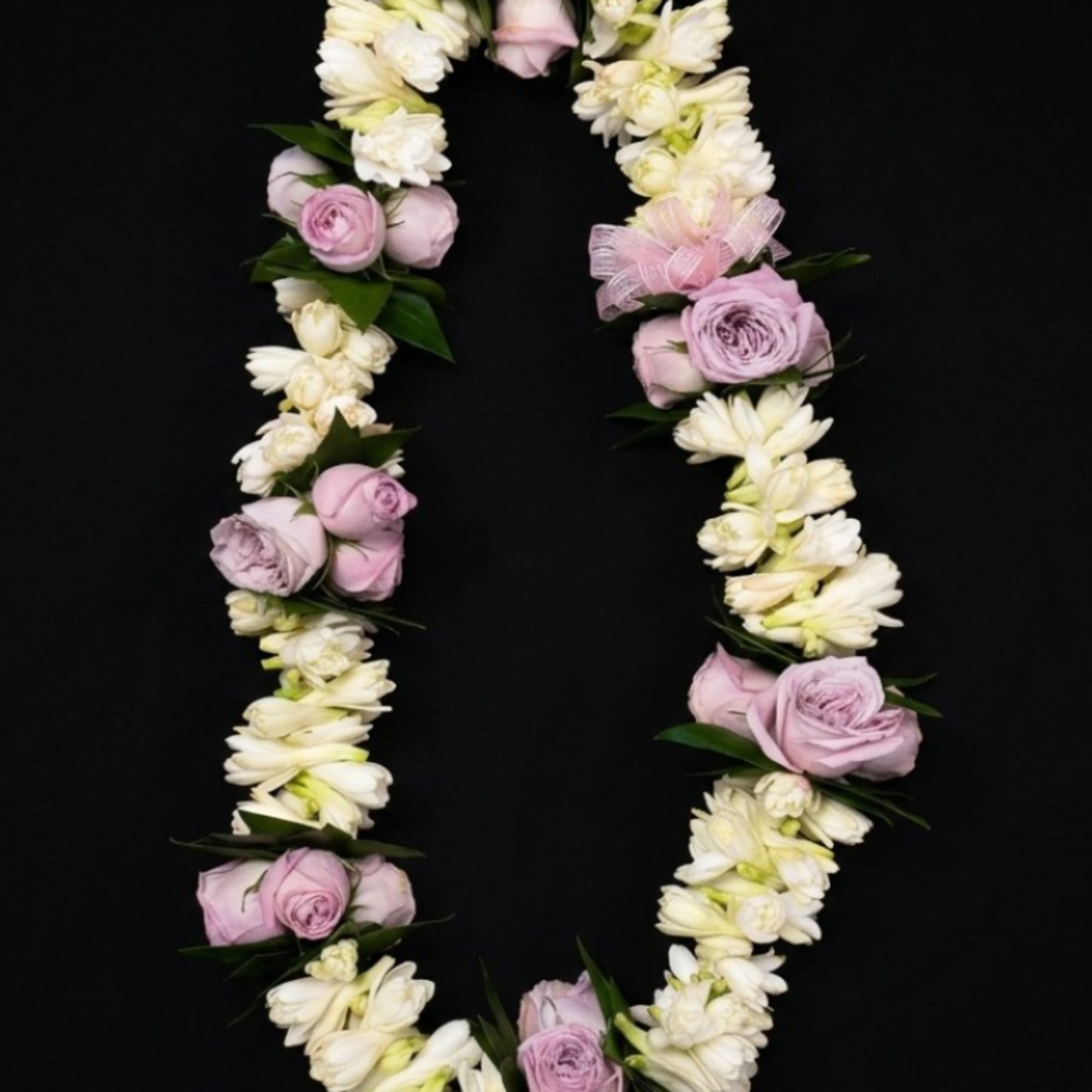 Pink roses and white flowers arranged in a floral garland on a black background