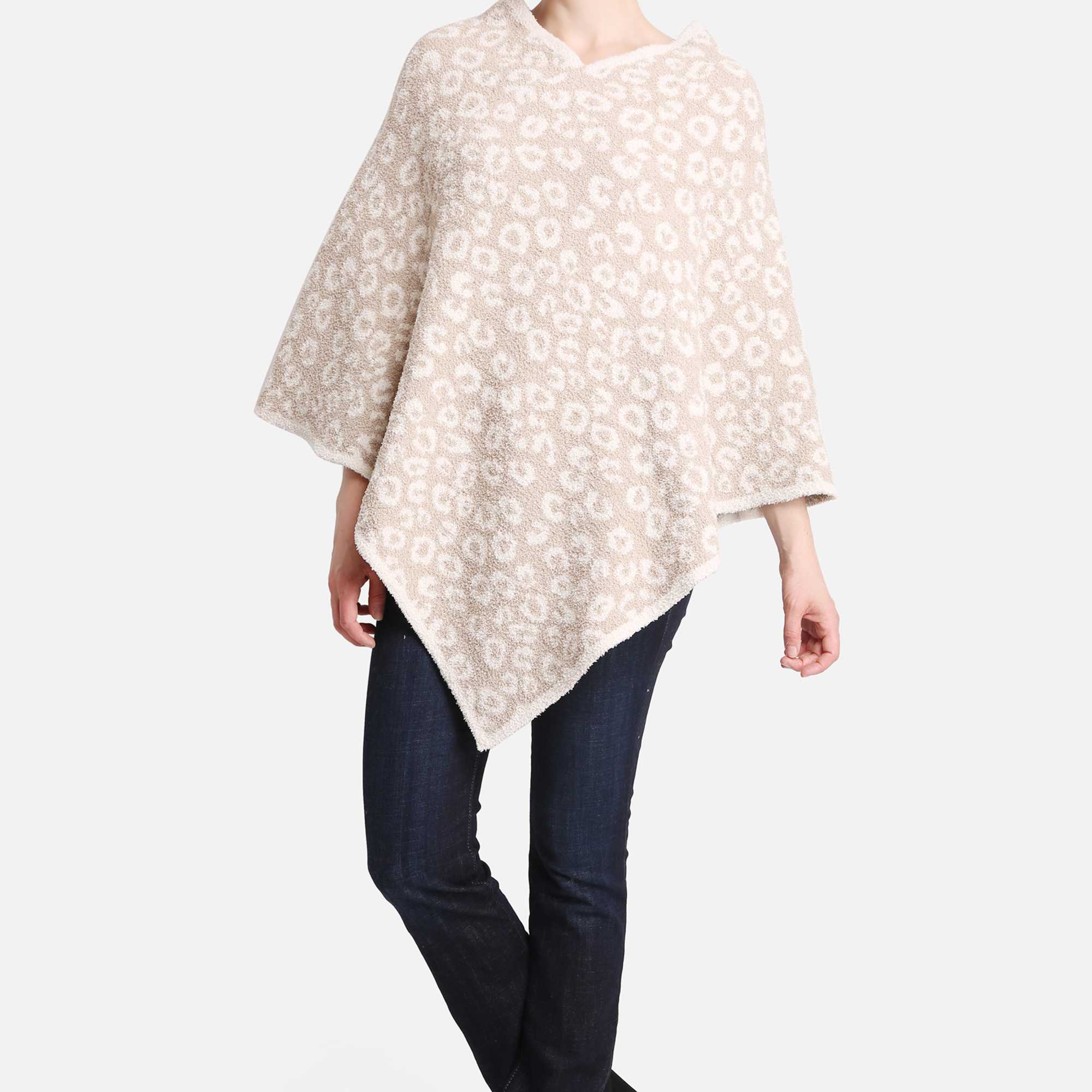Woman wearing a beige patterned poncho with dark jeans and black ankle boots