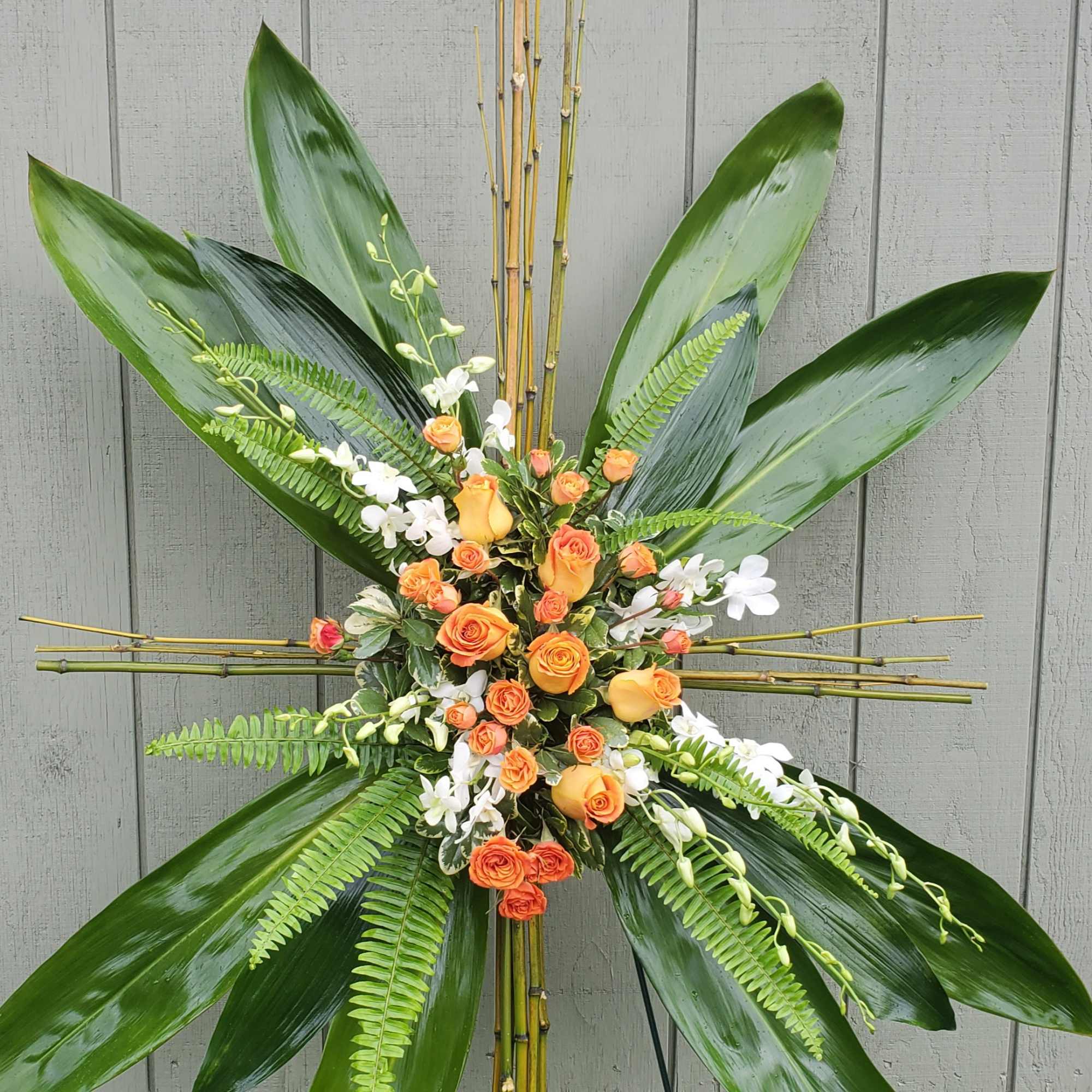 Orange roses and white orchids arranged with large tropical leaves