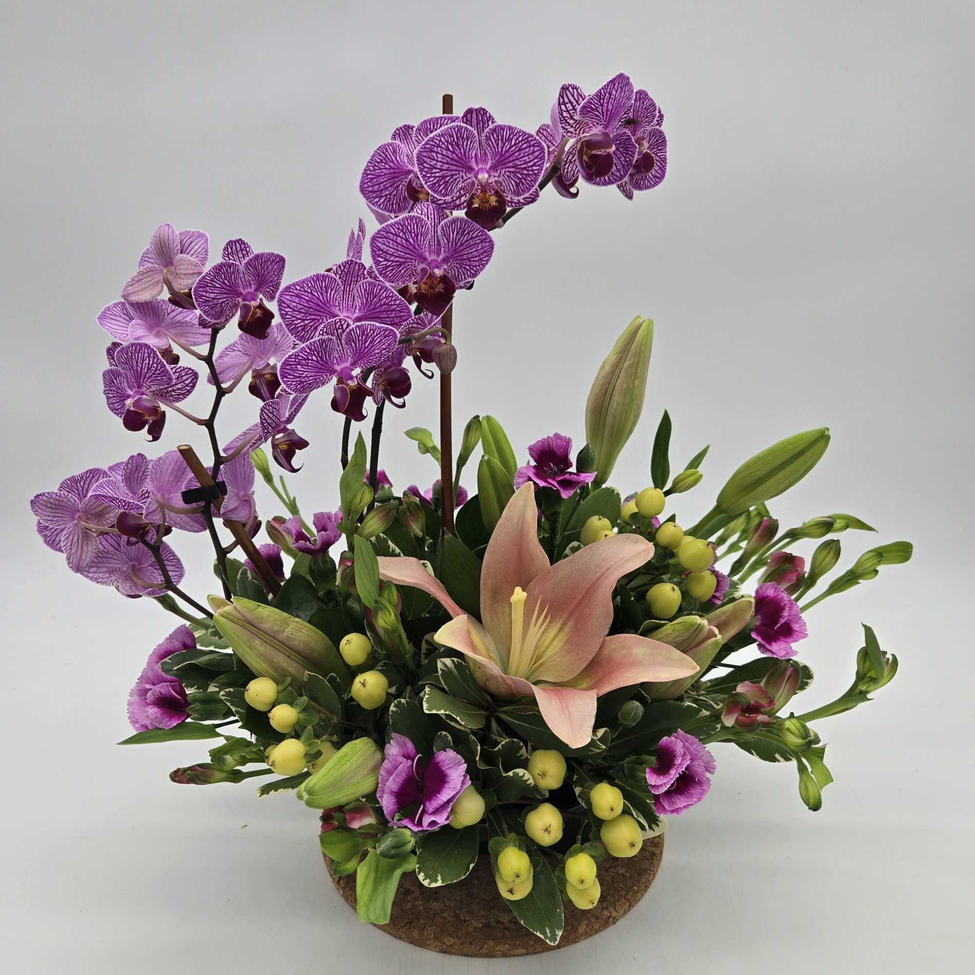 Purple orchids and a peach lily arranged in a low round container