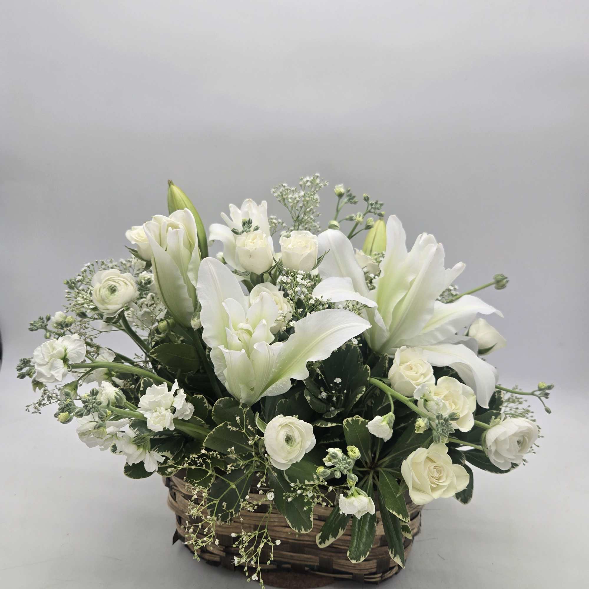 White floral arrangement in a woven basket with roses and lilies