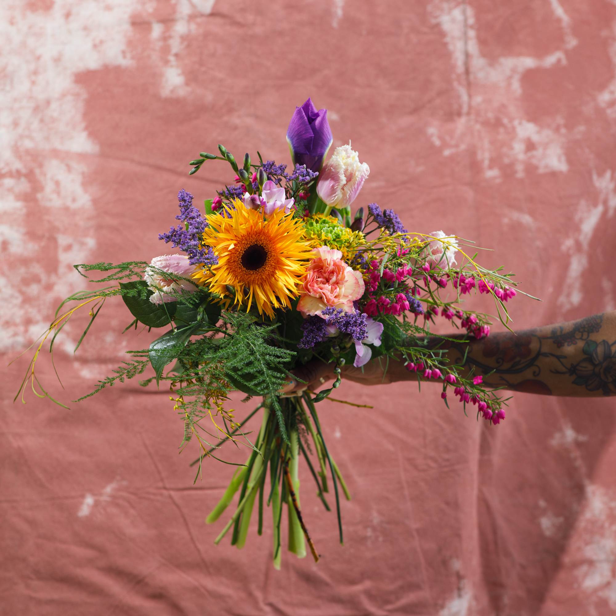 Handheld bouquet with a yellow sunflower and purple flowers