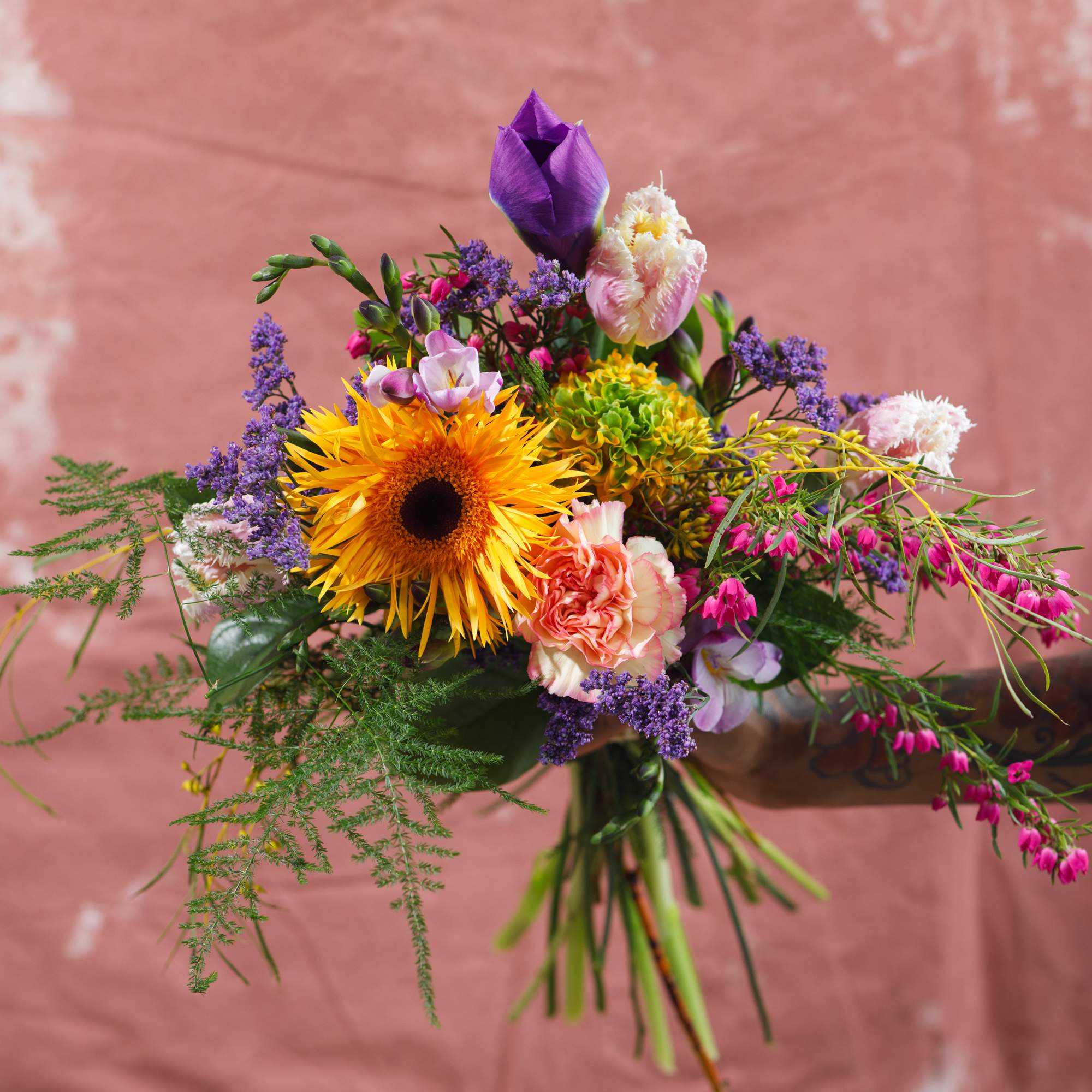 Handheld bouquet with a yellow sunflower, purple blooms, and pink flowers