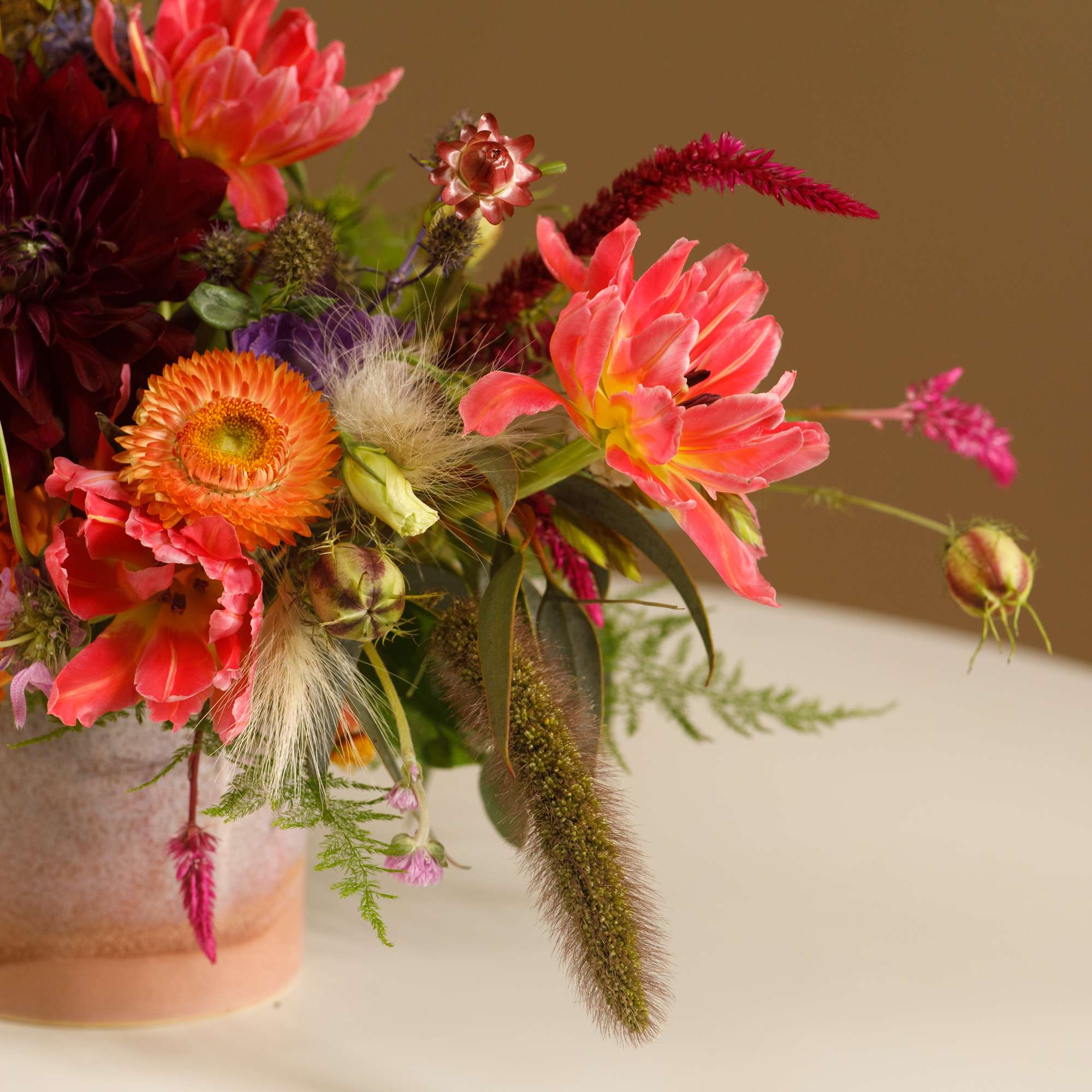 Mixed bouquet of orange, pink, and burgundy flowers in a ceramic vase