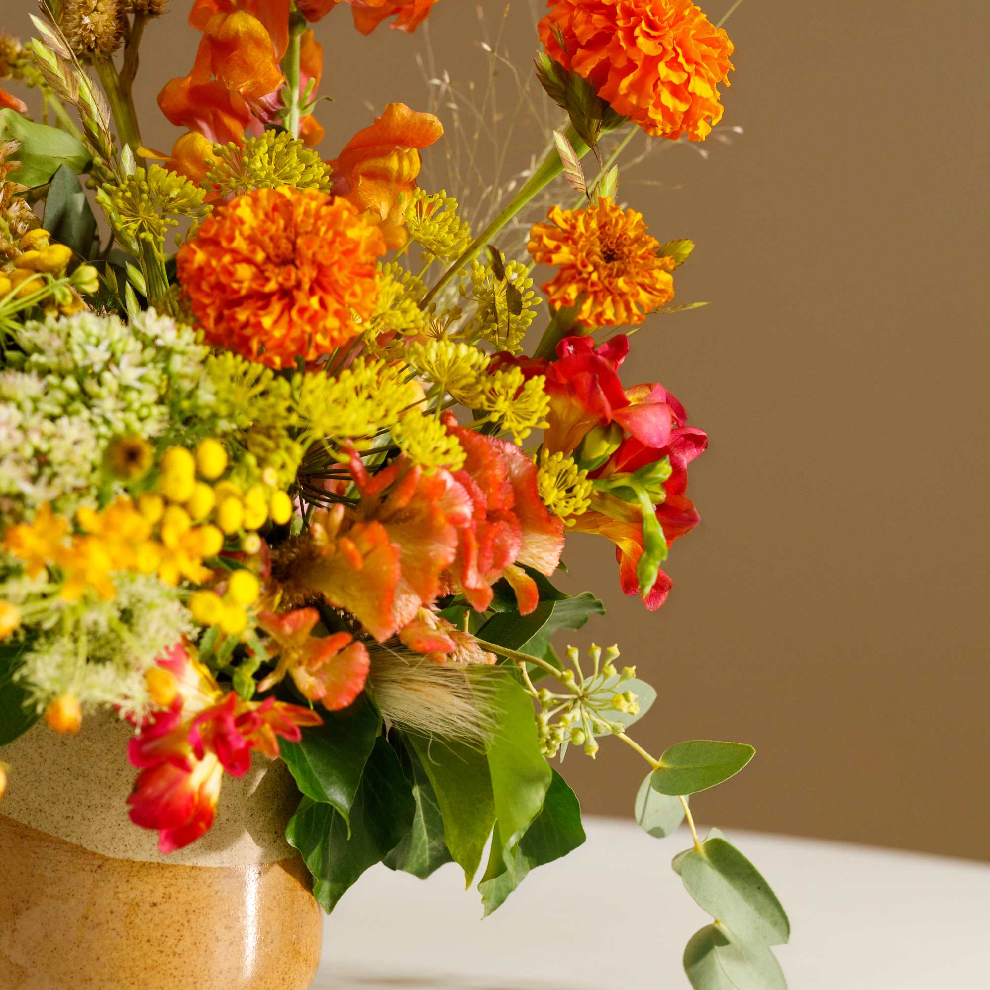 Bright orange and yellow mixed bouquet in a tan ceramic vase
