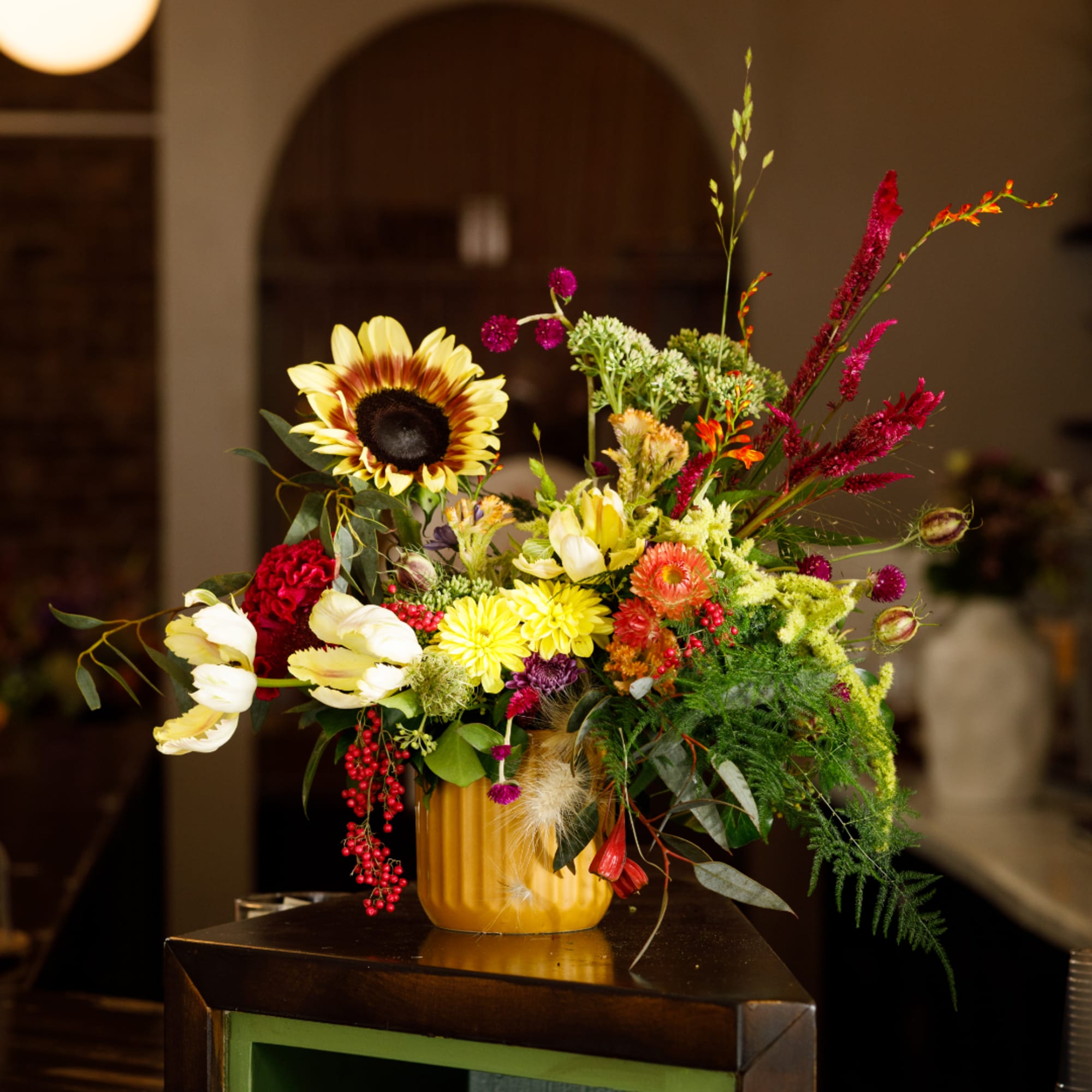 Colorful mixed flower arrangement in a yellow vase with a sunflower and tulips