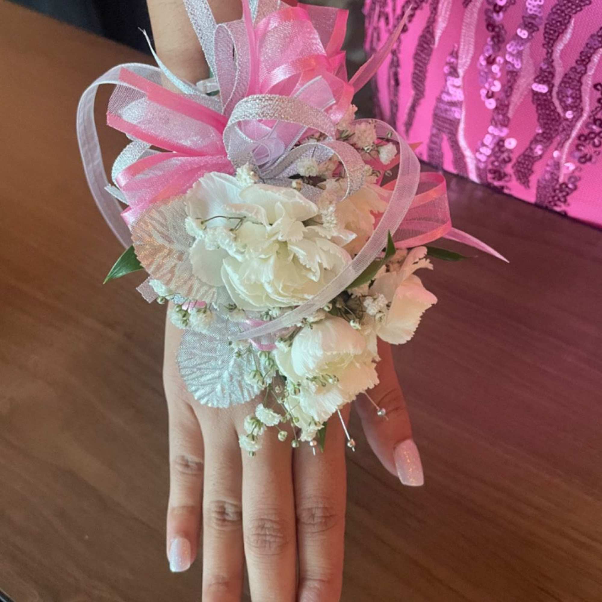 White floral wrist corsage with pink ribbon on a hand