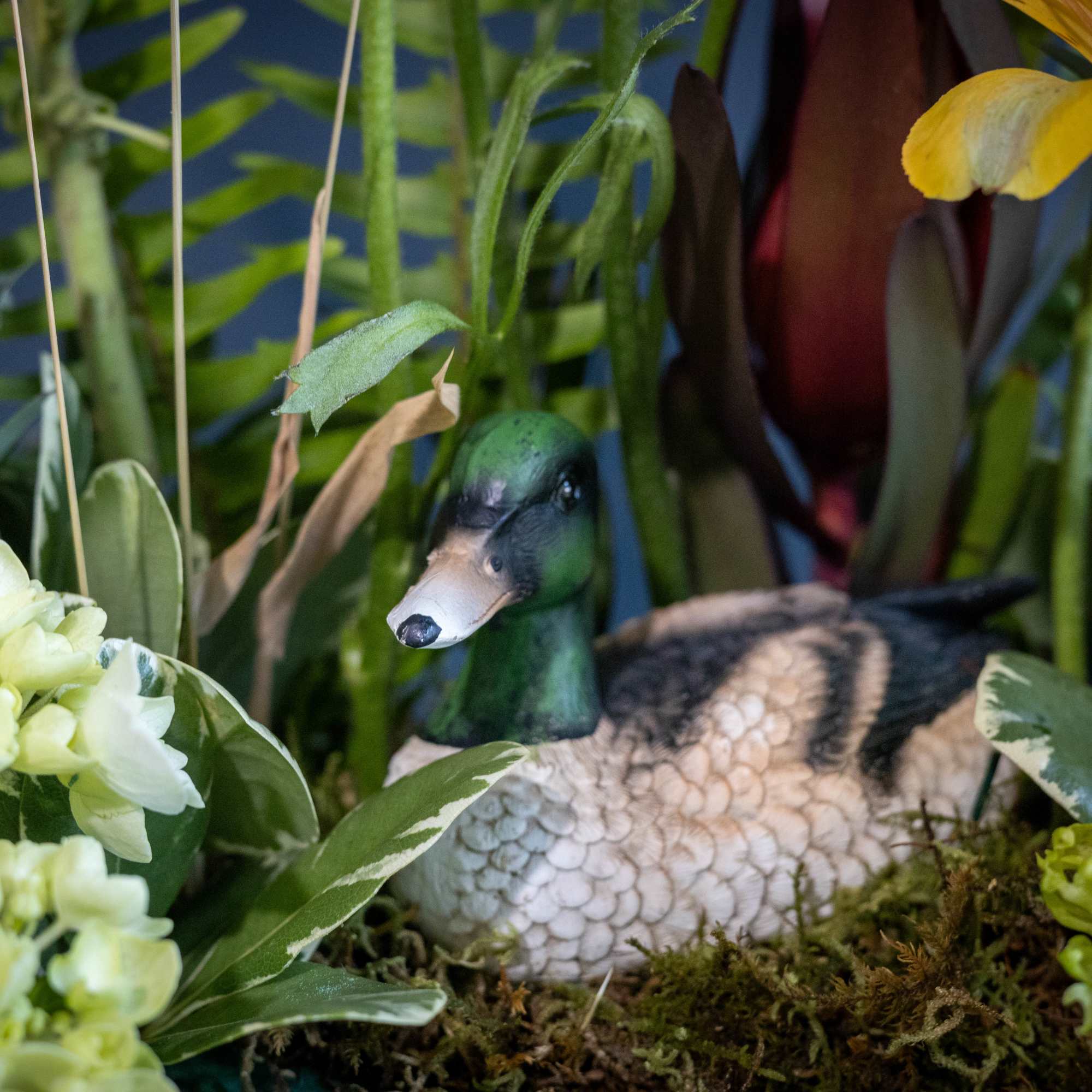 Duck figurine nestled among flowers and greenery