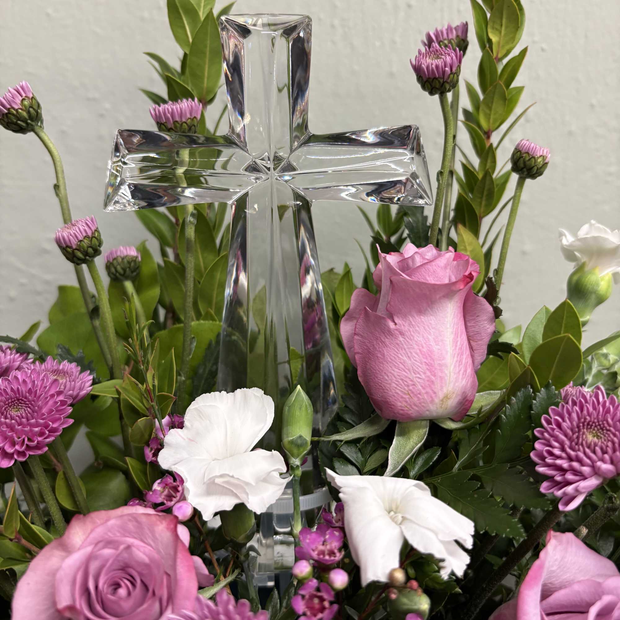 Pink roses and white flowers arranged around a clear glass cross