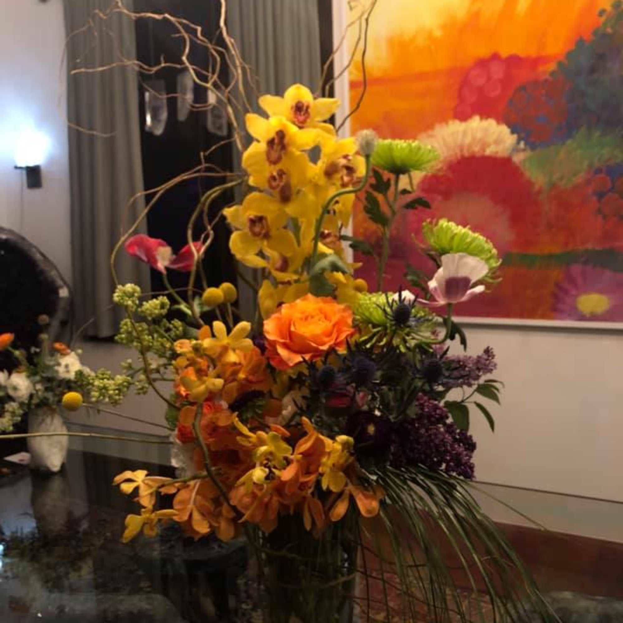 Tall mixed floral arrangement with yellow orchids and orange roses in a glass vase