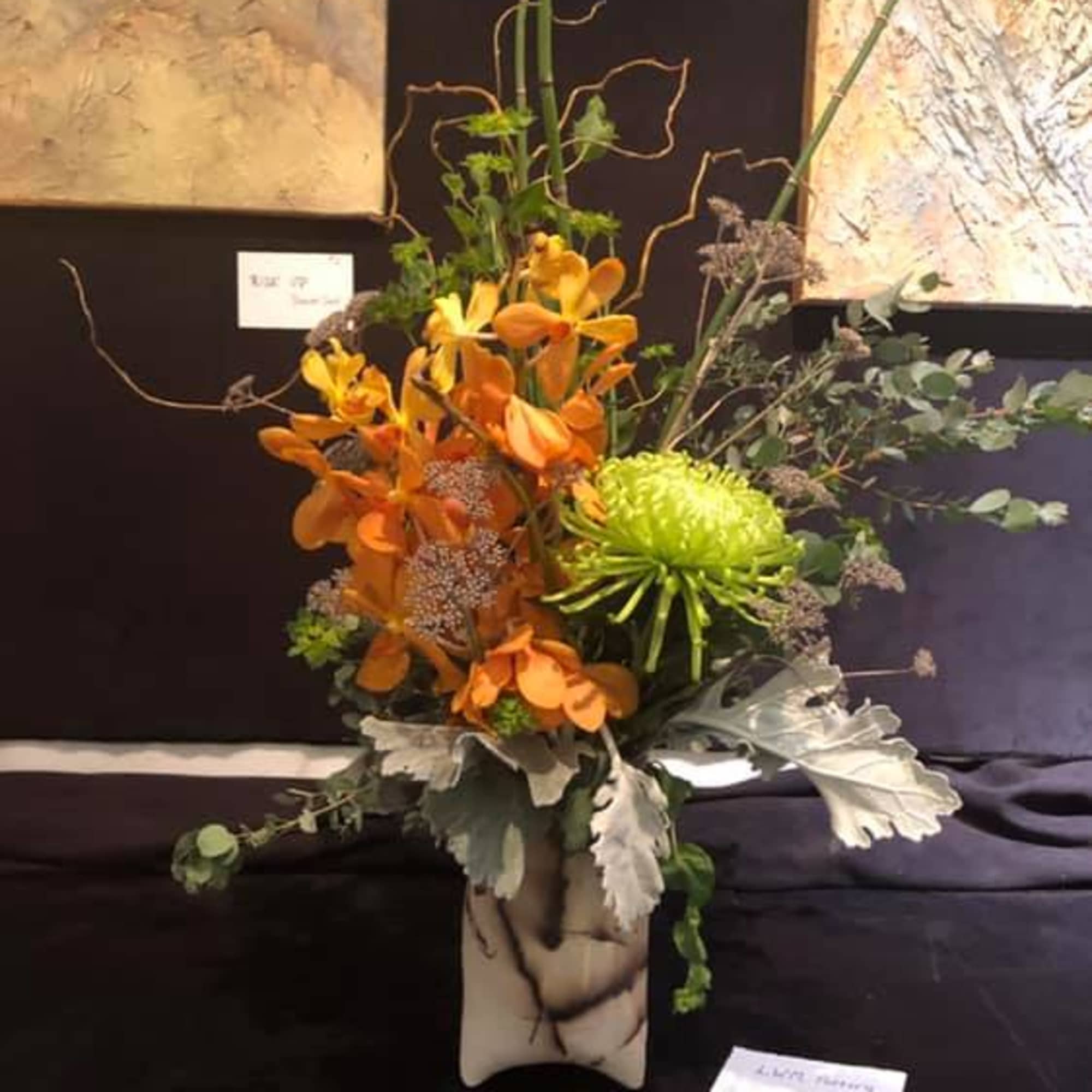 Tall floral arrangement with orange orchids and a green chrysanthemum in a vase