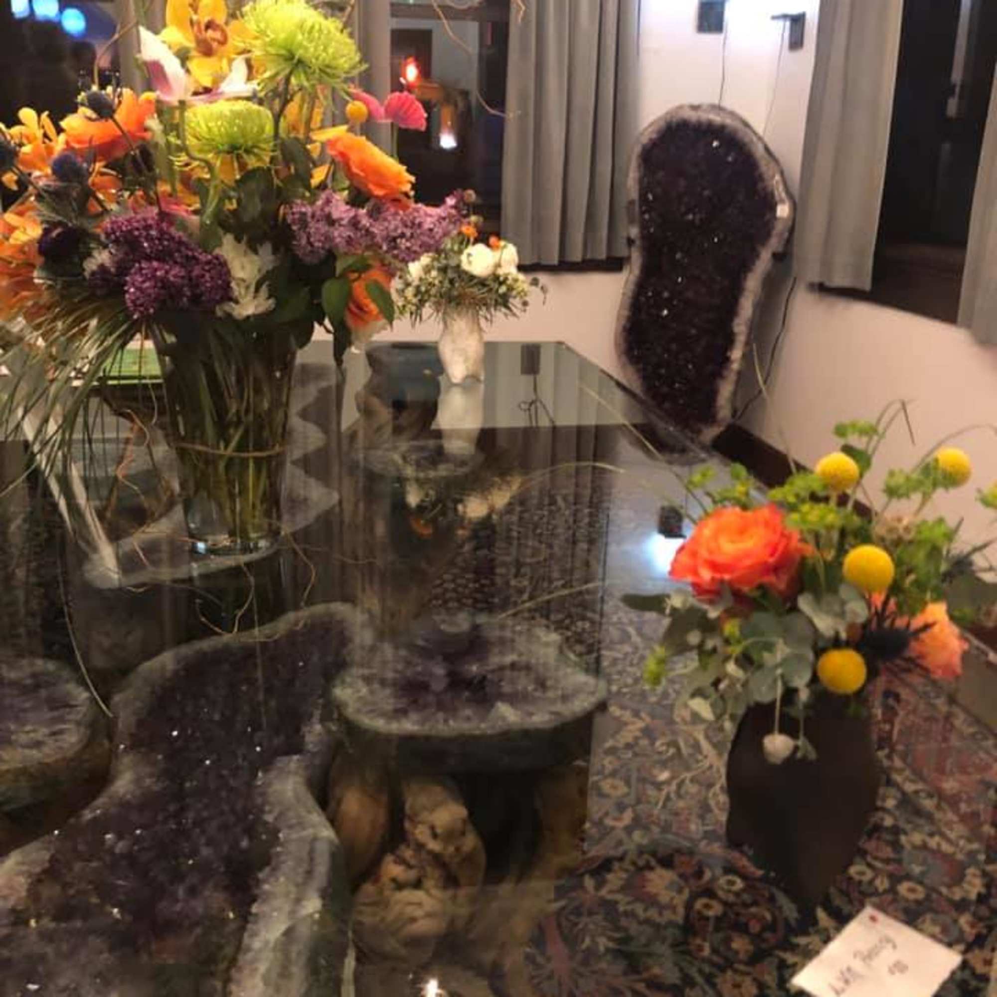 Tall floral arrangement with orange, yellow, and purple blooms in a glass vase