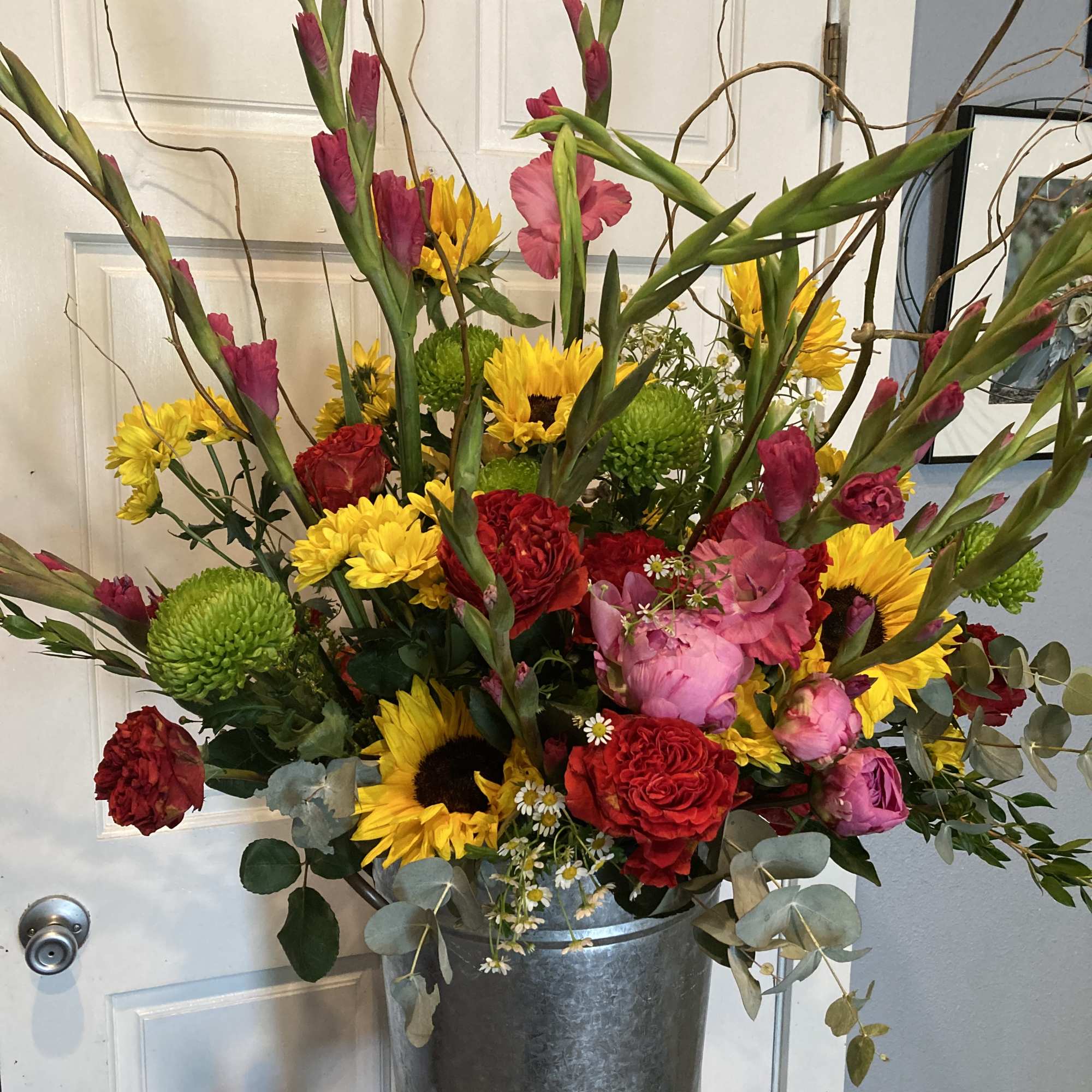 Tall mixed bouquet in a metal vase with sunflowers, roses, and pink blooms