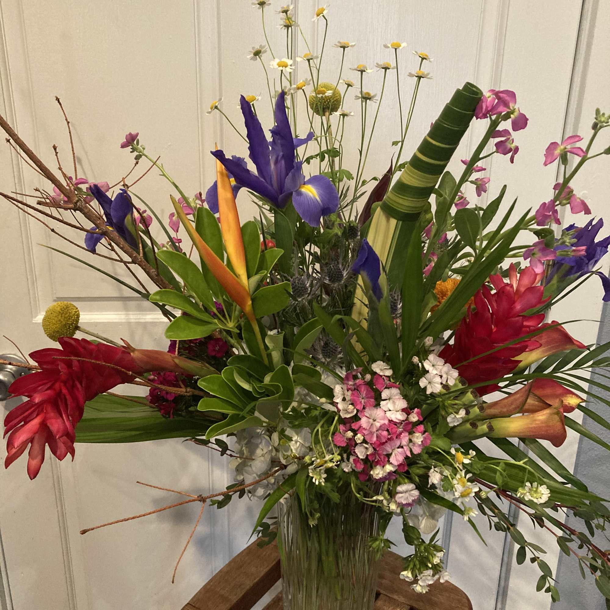 Tall tropical bouquet with red, purple, pink, and orange flowers in a glass vase