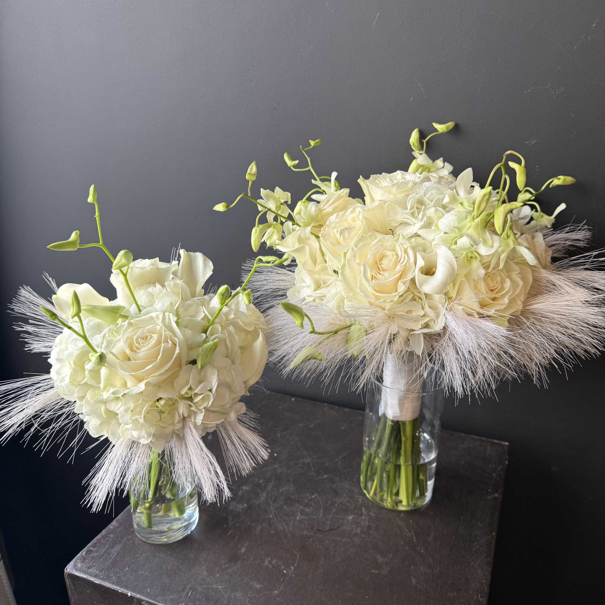 Two ivory bridal bouquets in clear glass vases with feathery accents