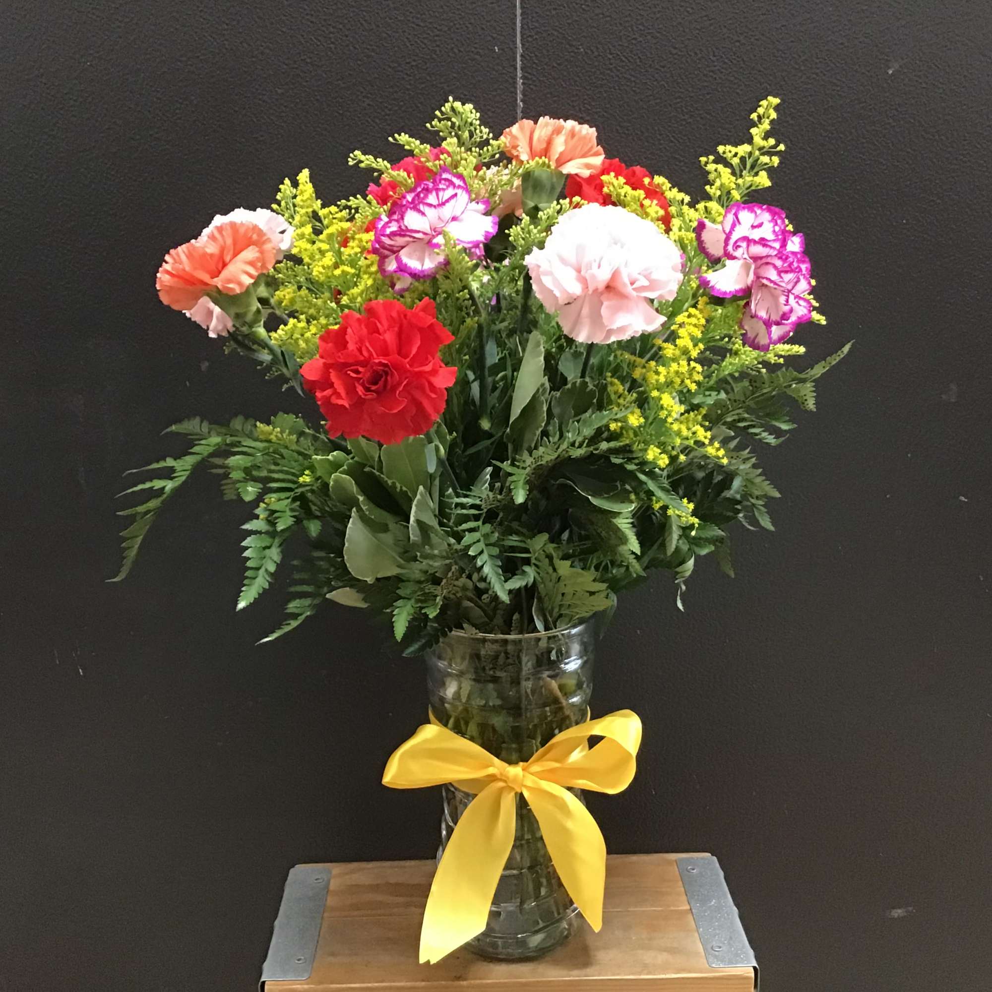 Mixed carnation bouquet in a glass vase with a yellow ribbon