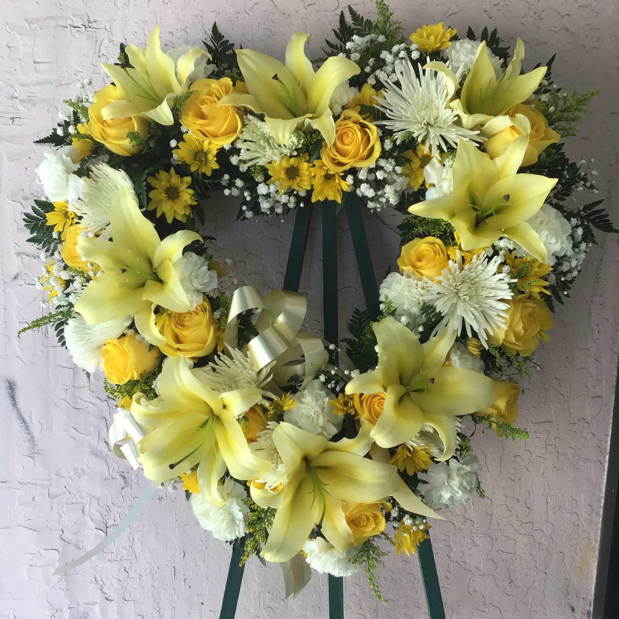 Heart-shaped floral wreath with yellow lilies, roses, and white flowers