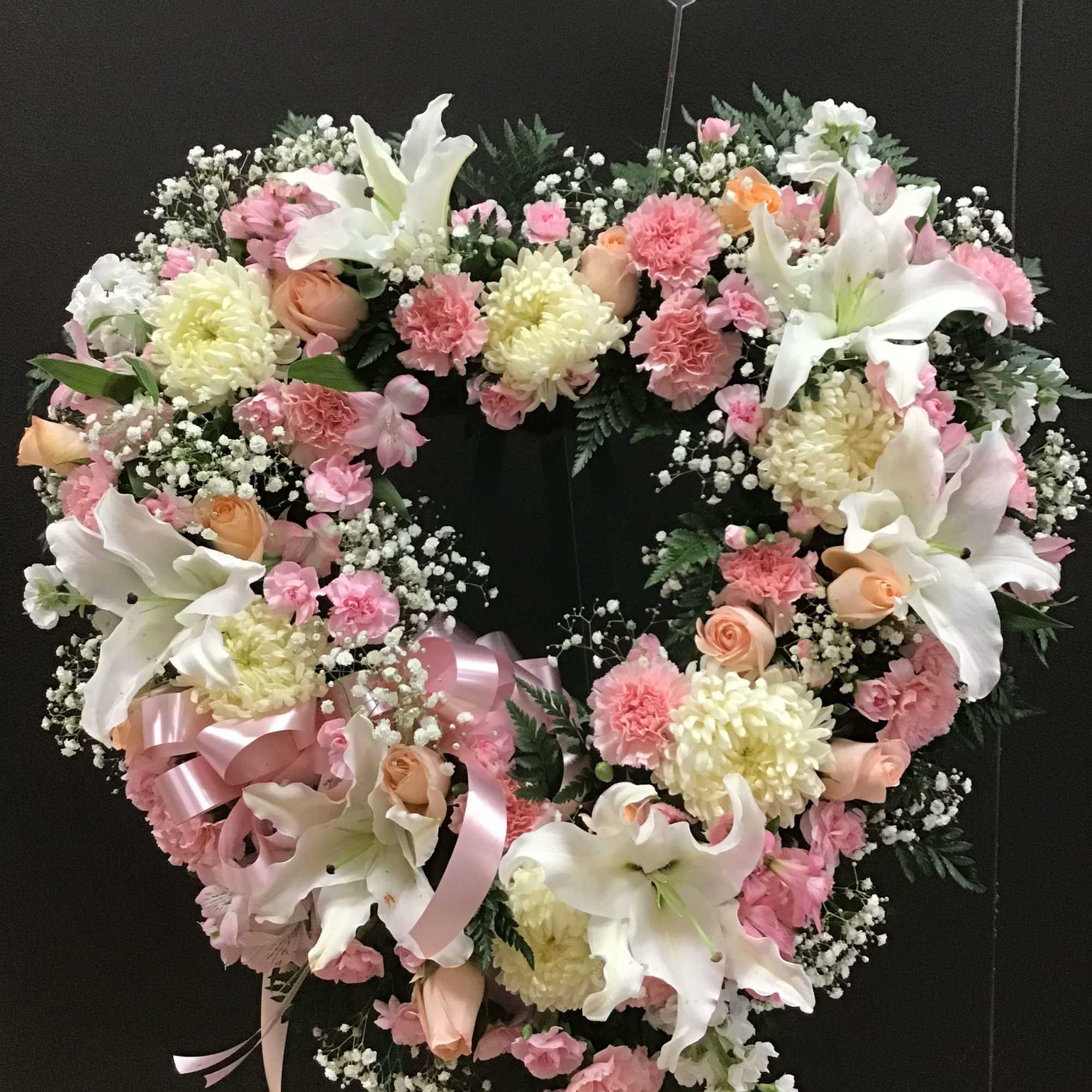 Heart-shaped floral wreath with white lilies, pink carnations, and roses