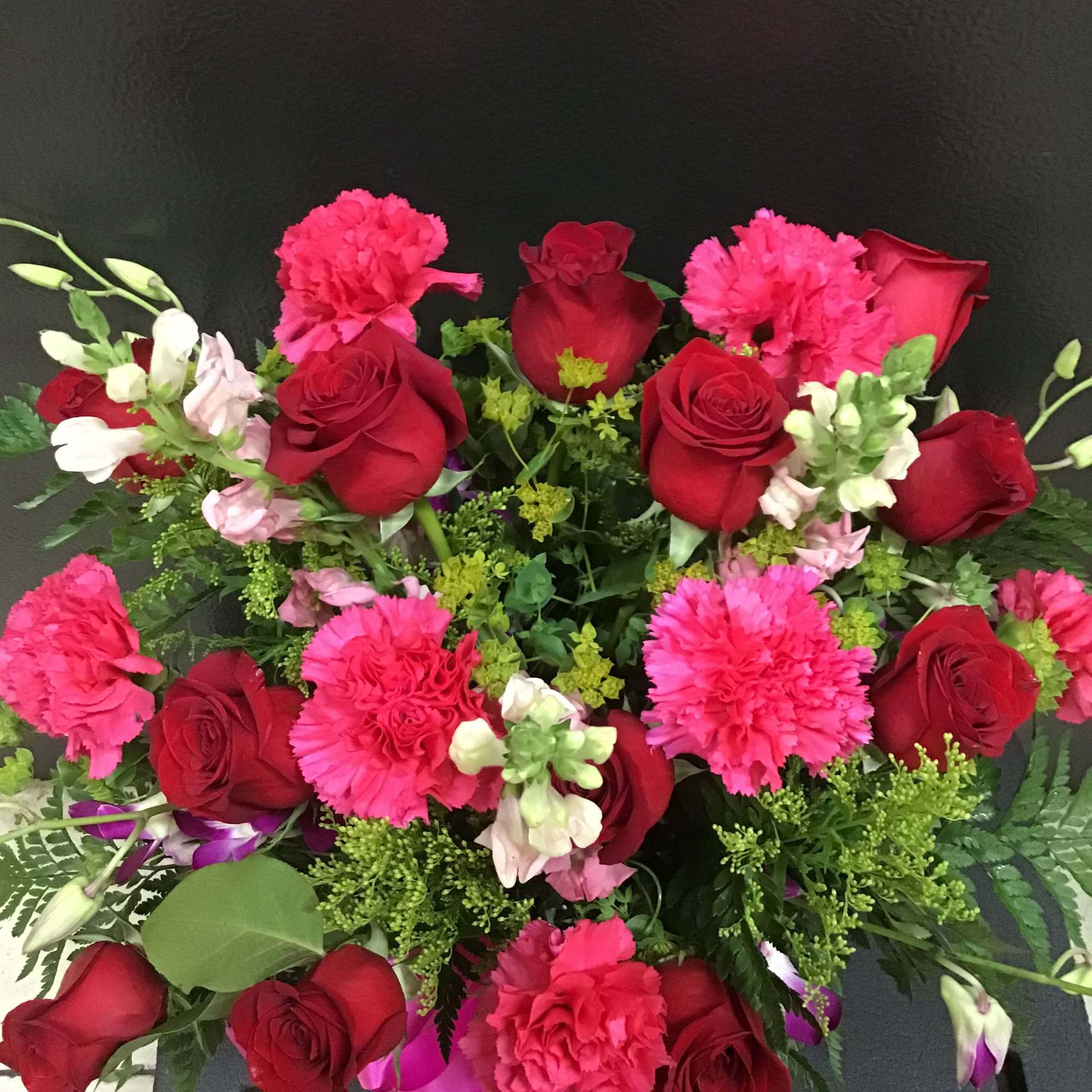 Bouquet of red roses and hot pink carnations with mixed greenery