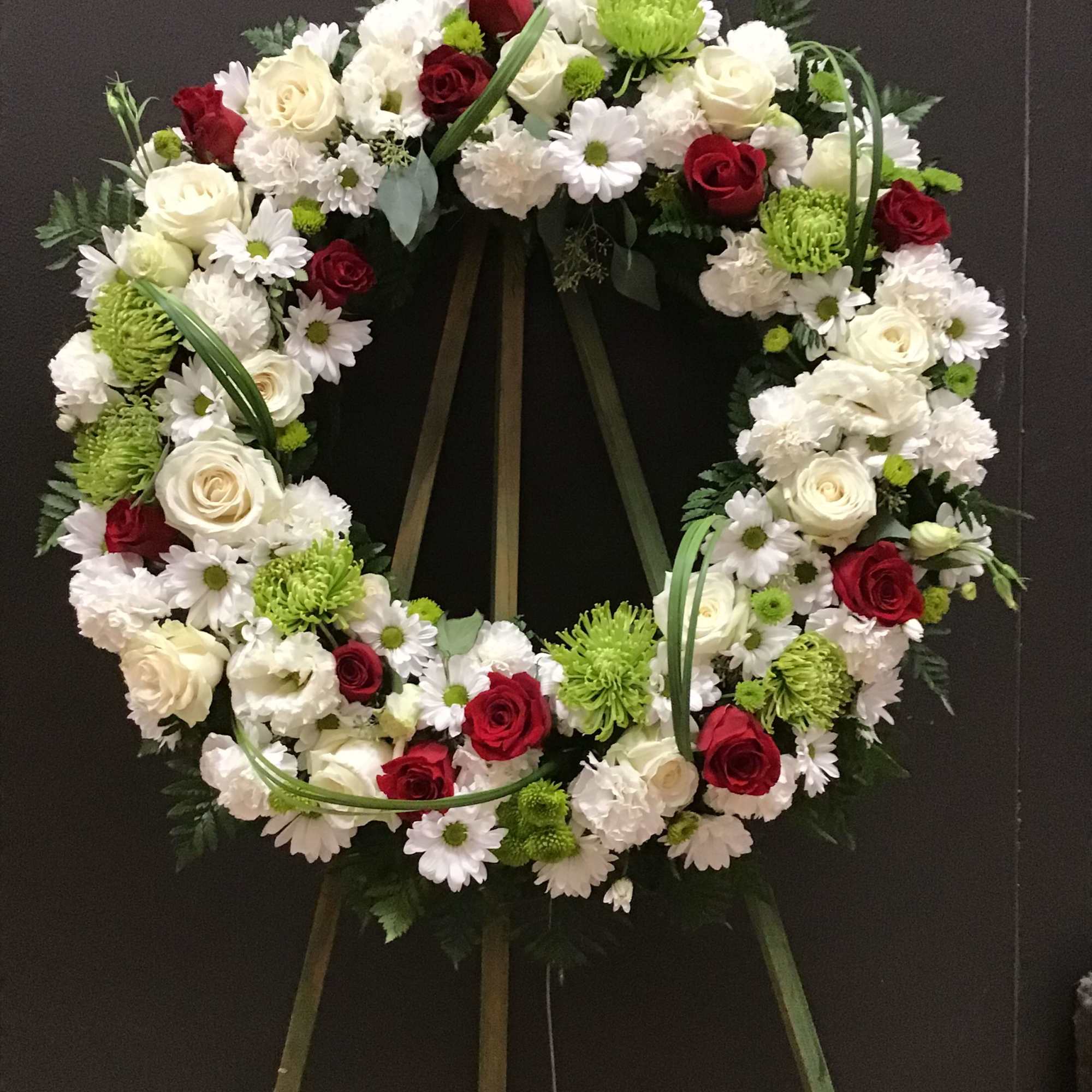 Circular floral wreath with red and white flowers on a stand