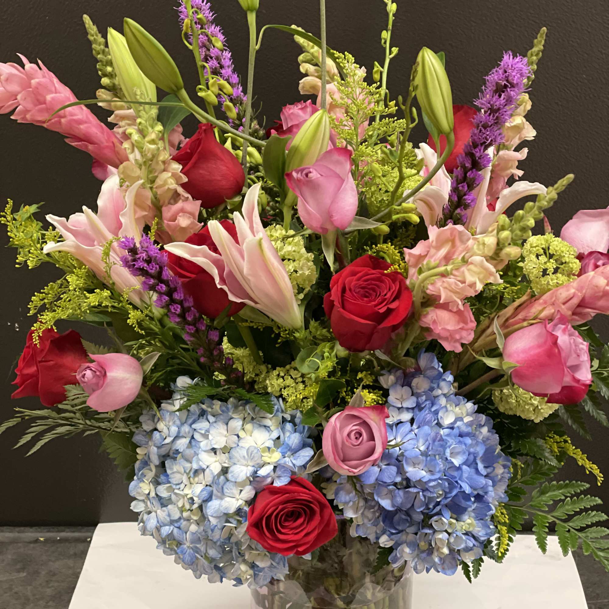 Mixed bouquet of roses, lilies, and hydrangeas in a clear glass vase