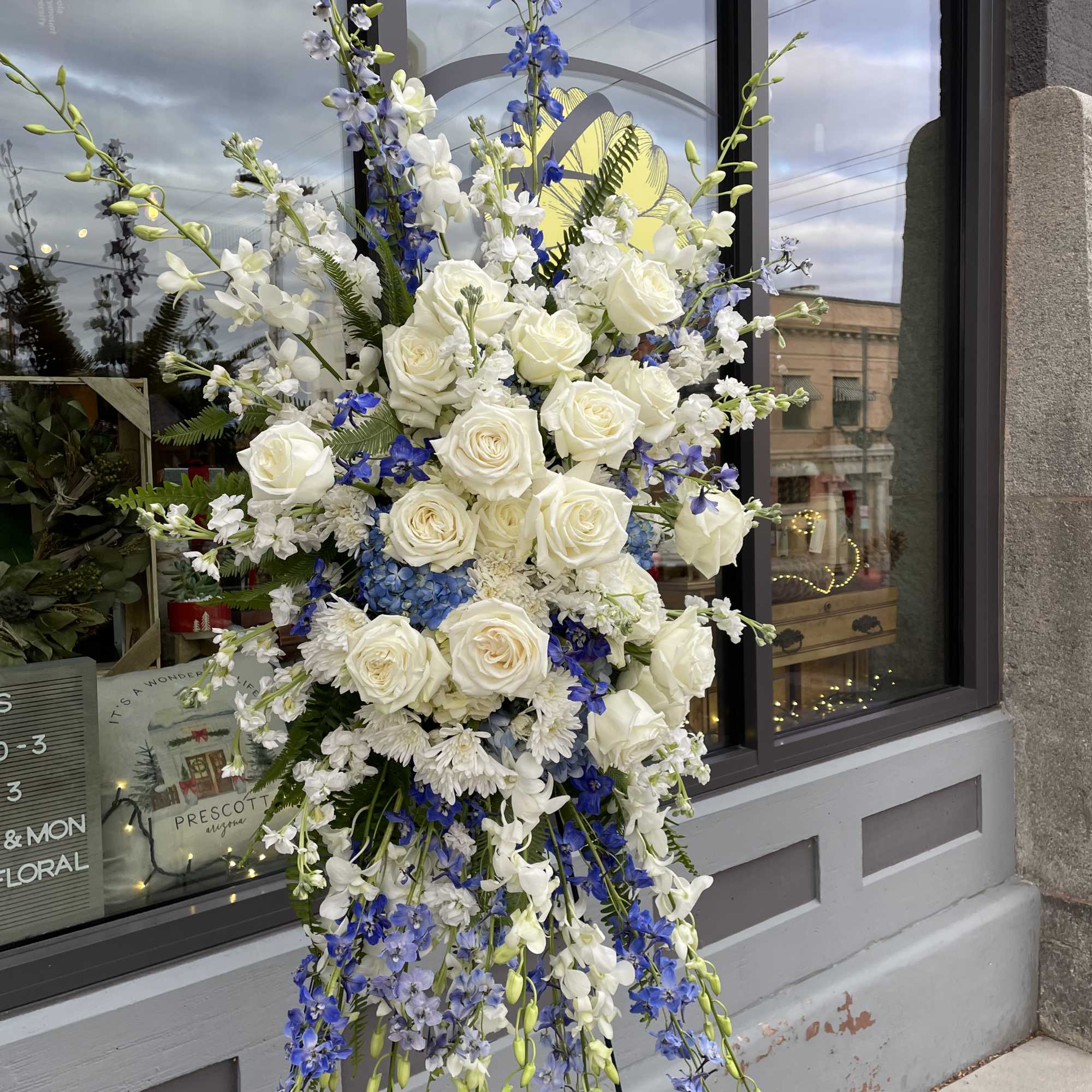 Tall floral spray with white roses and blue flowers on a stand