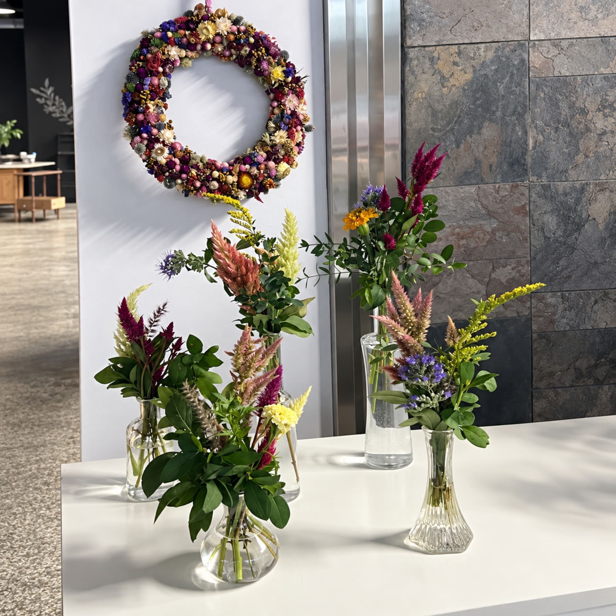 Small mixed flower arrangements in clear glass vases beside a floral wreath.