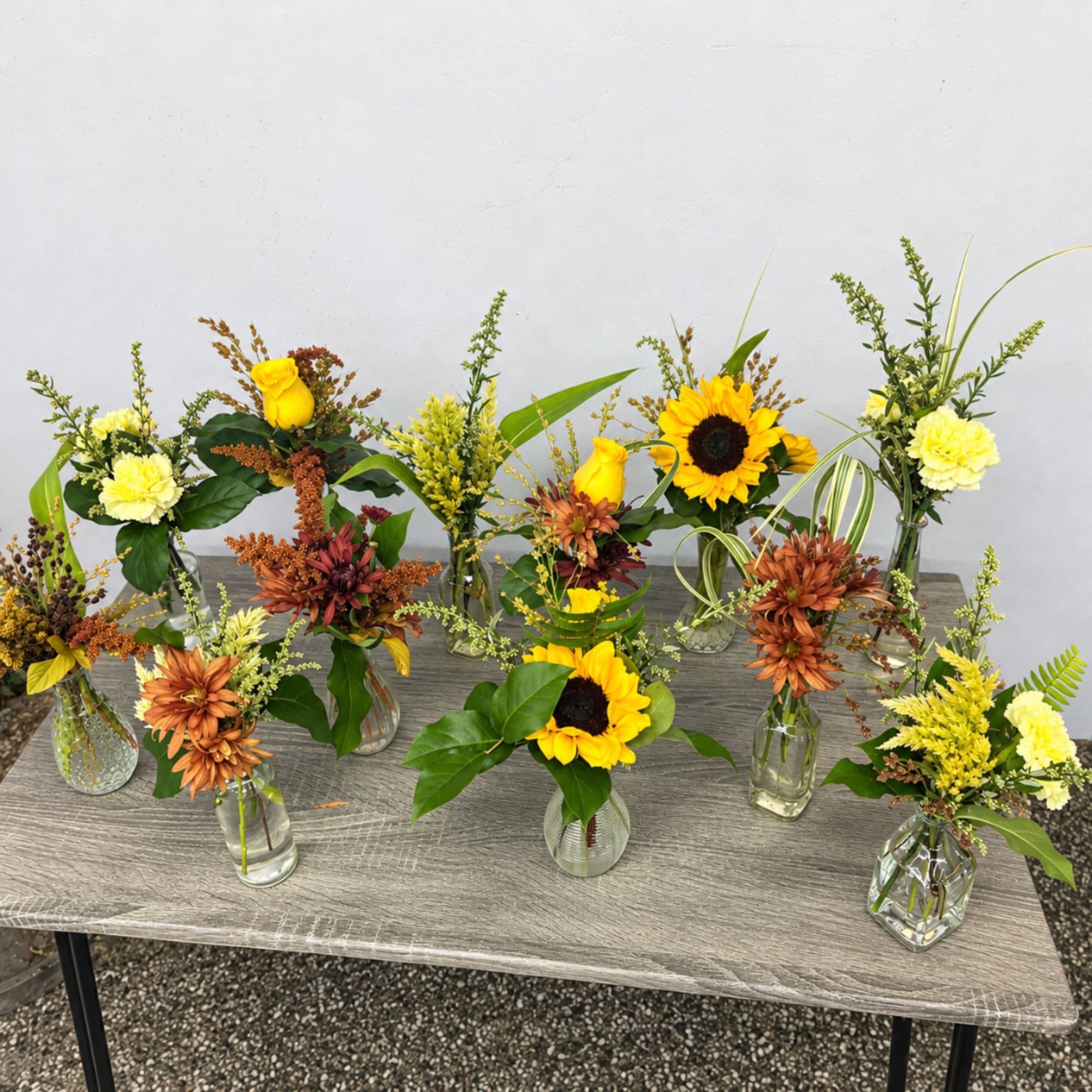Assorted small floral arrangements in glass vases with sunflowers and carnations