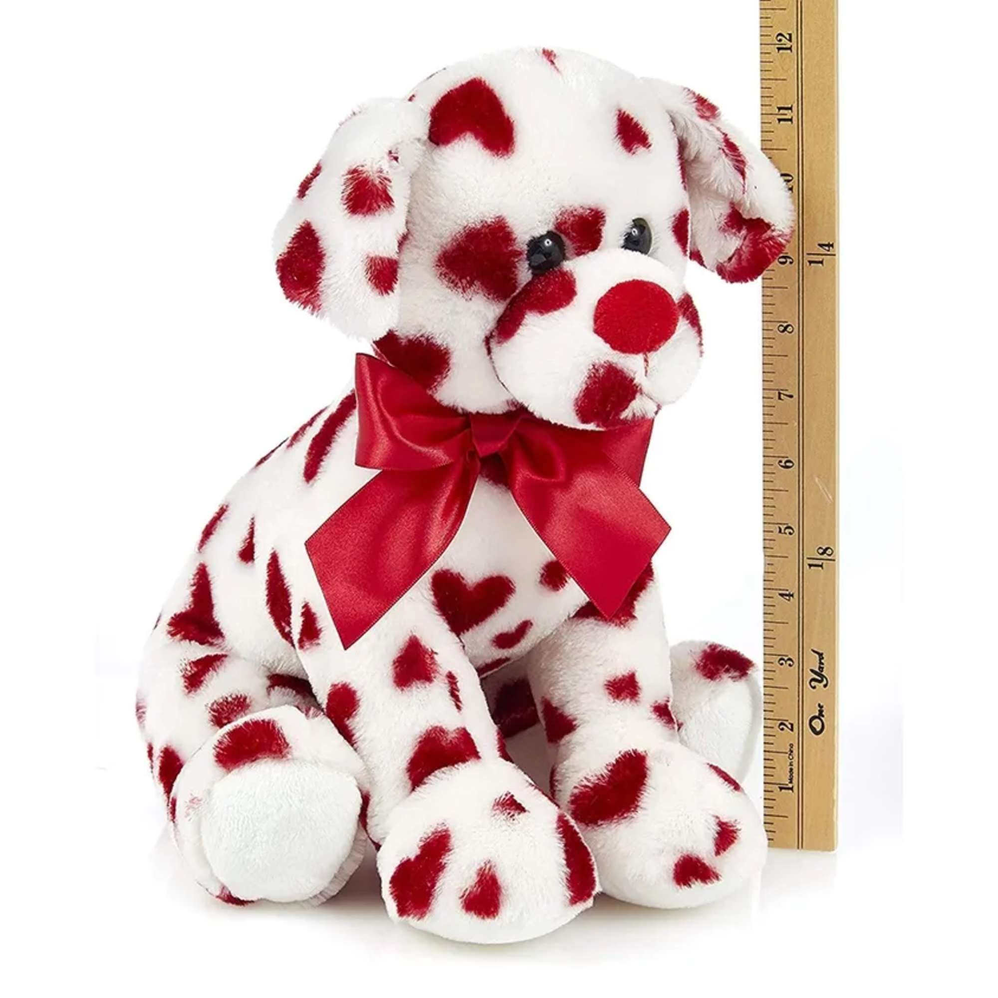 Plush Dalmatian puppy with a red satin bow beside a ruler