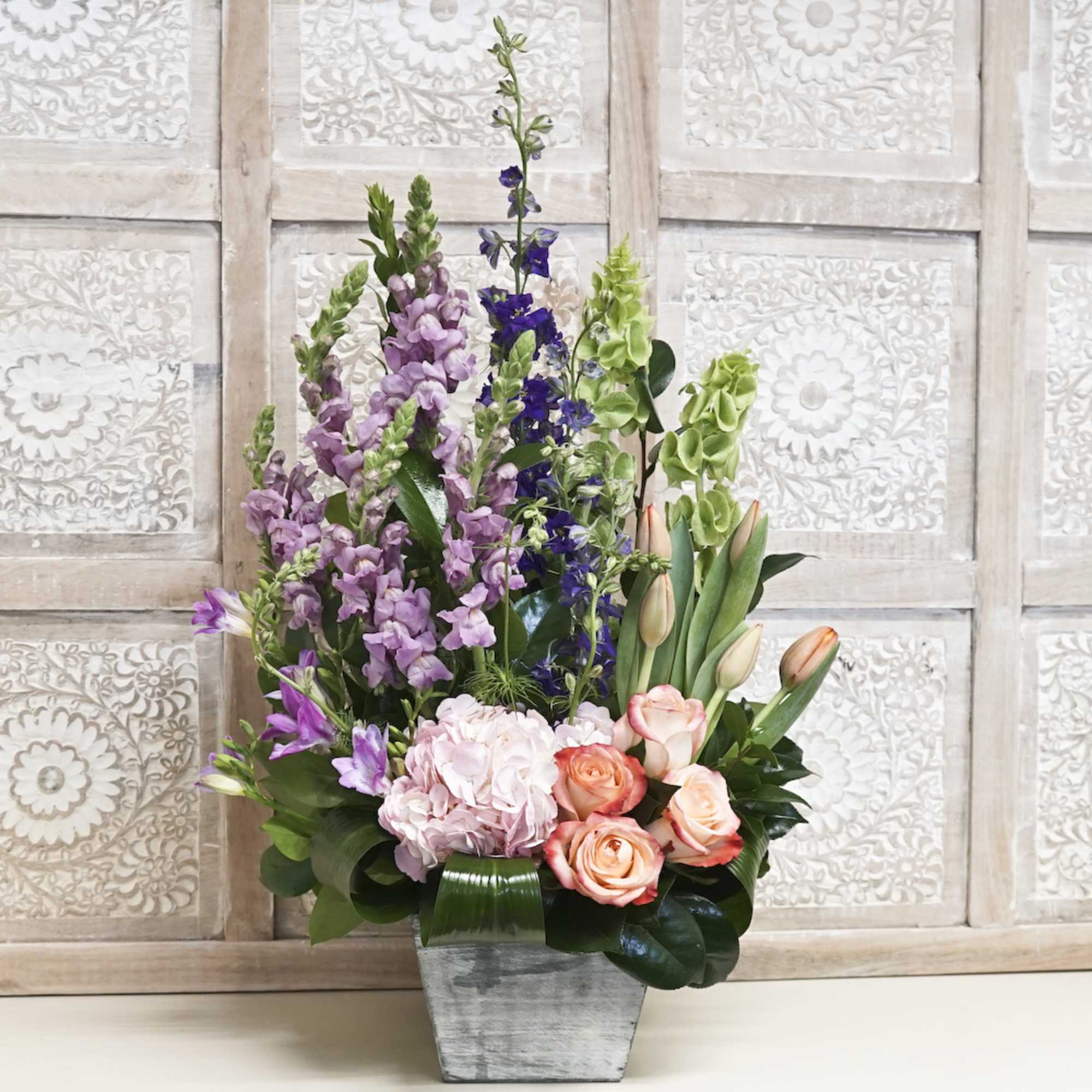 Tall mixed bouquet with roses, tulips, and purple spikes in a gray vase