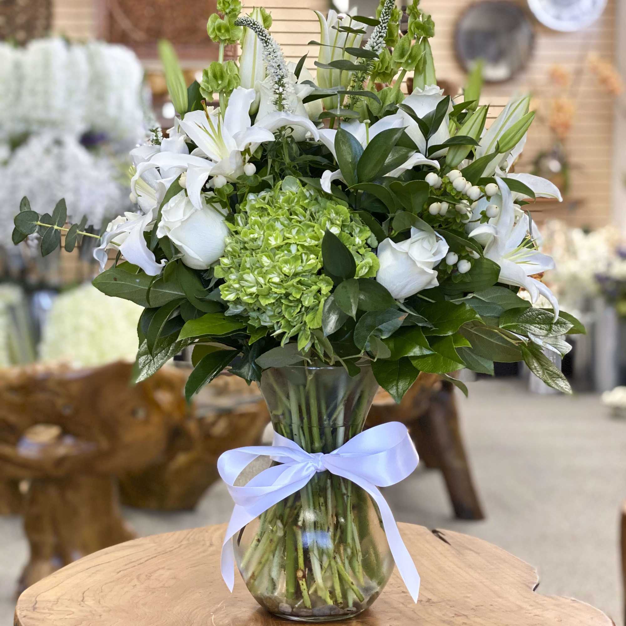 White lilies and roses in a glass vase with a blue ribbon