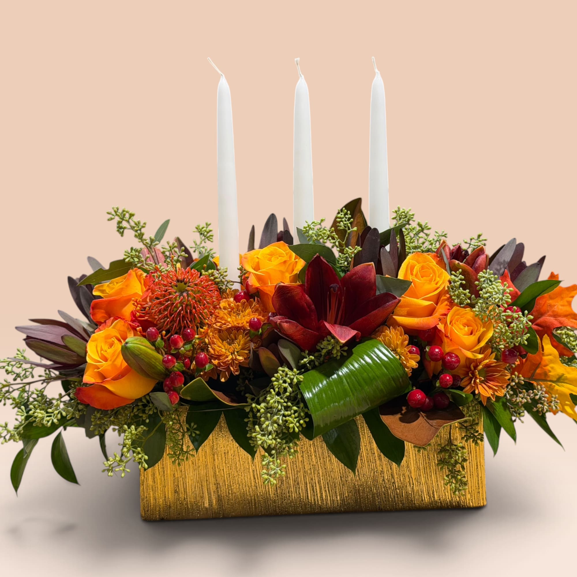 Floral centerpiece with three white candles in a gold box