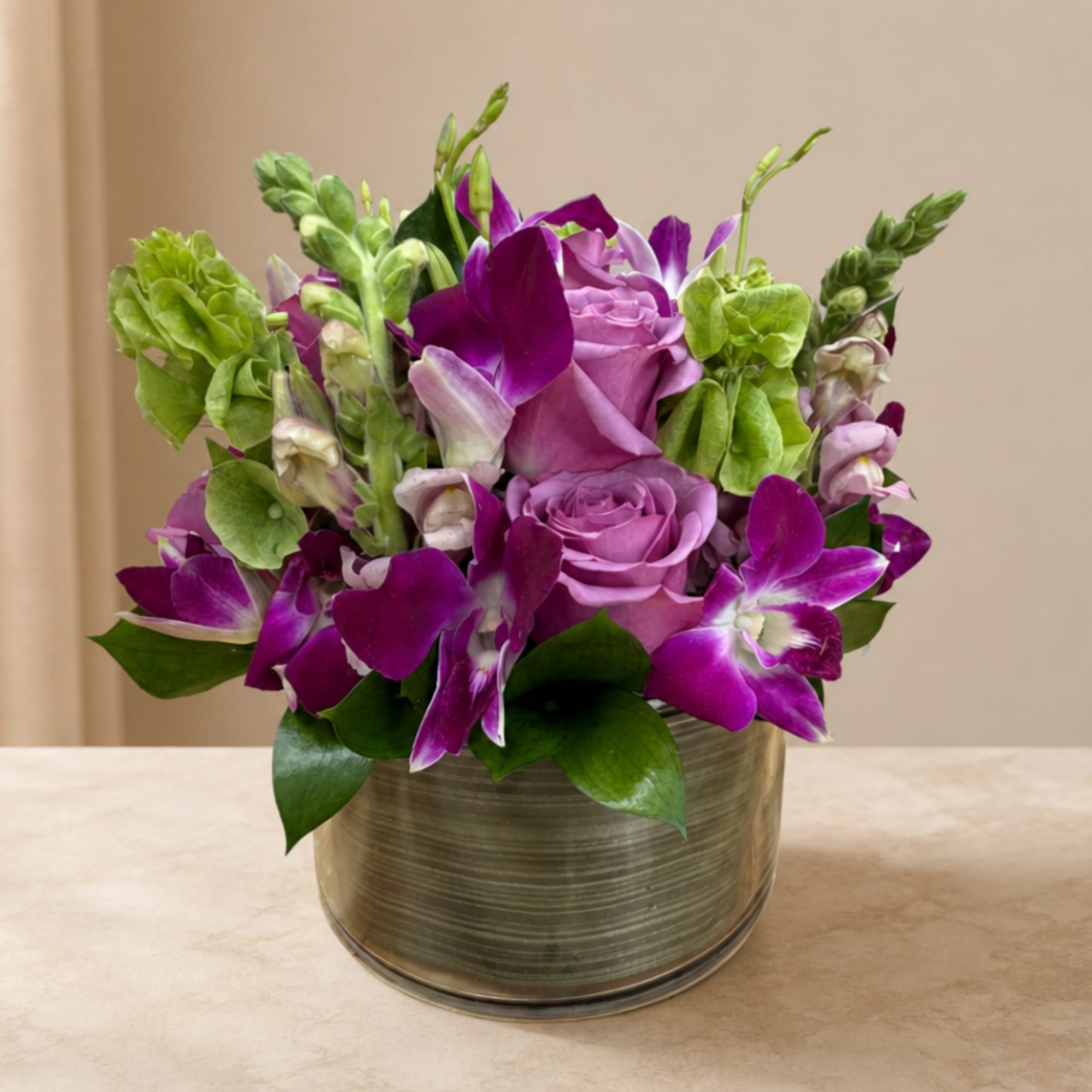 Purple roses and orchids arranged in a round metal vase
