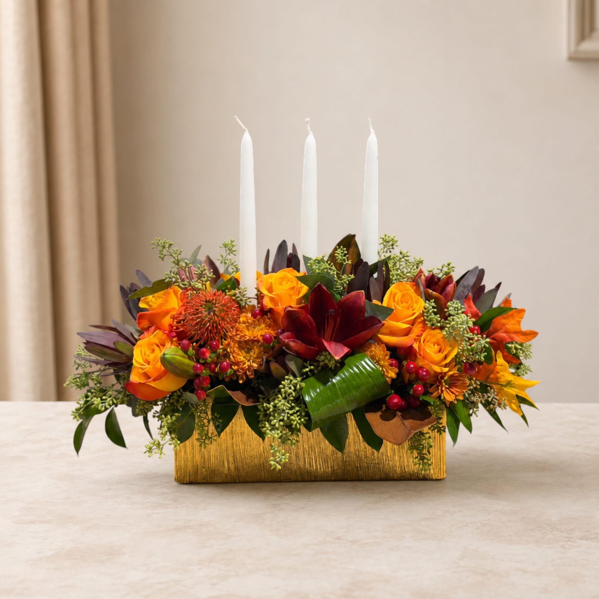 Orange and red floral centerpiece with three white candles in a gold container