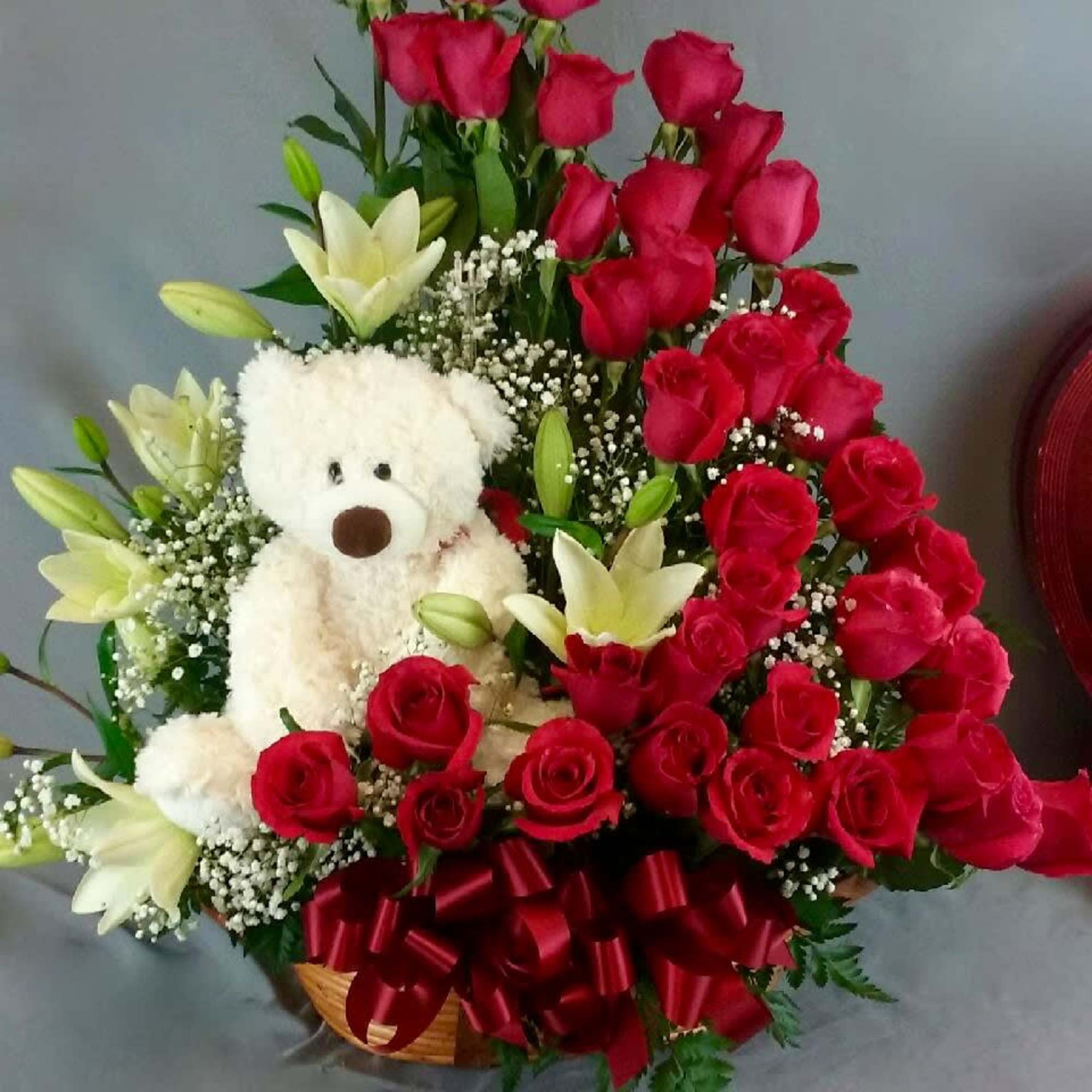 Red roses and white lilies arranged with a teddy bear in a basket, photo 2 of 2