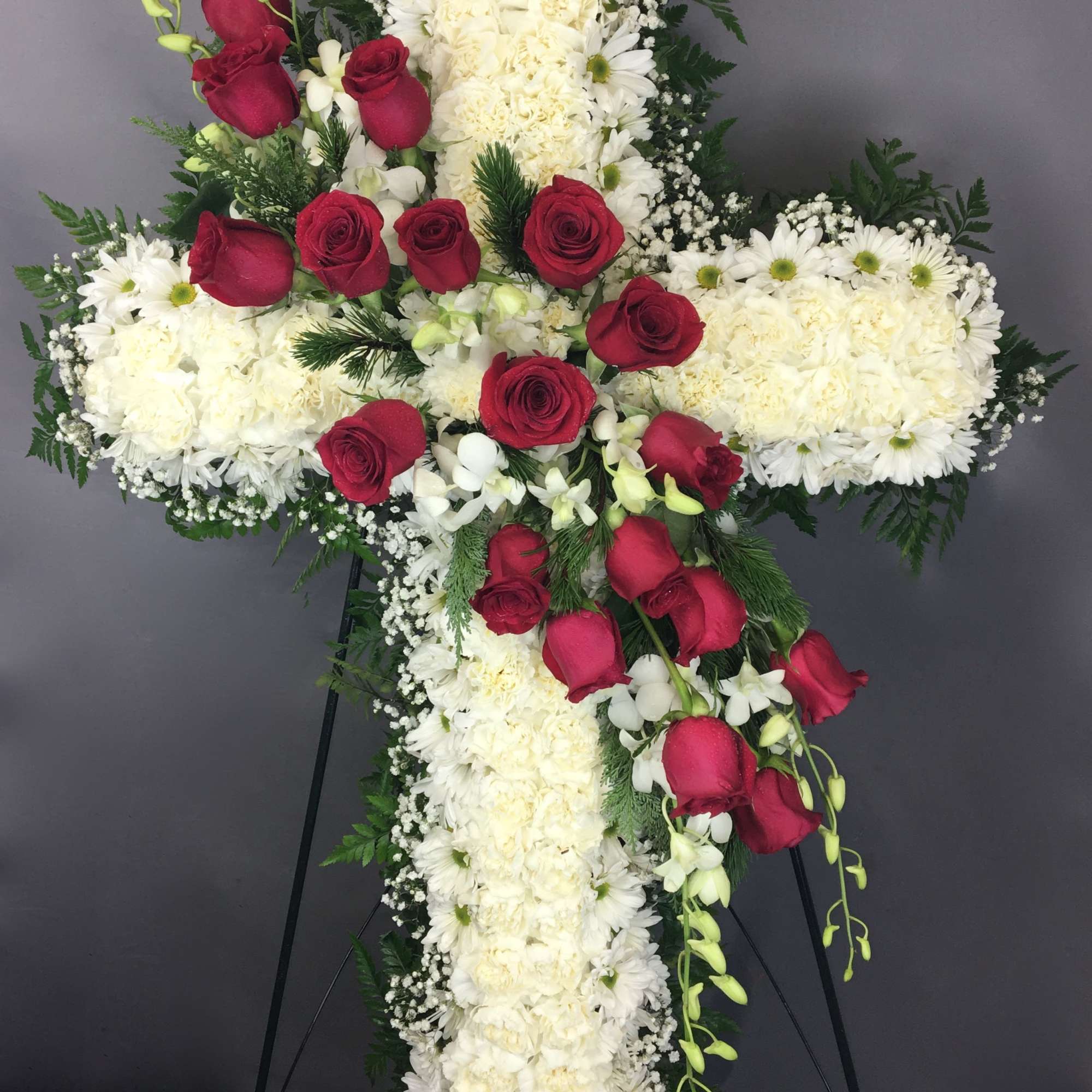 Cross-shaped floral tribute with white flowers and red roses on an easel